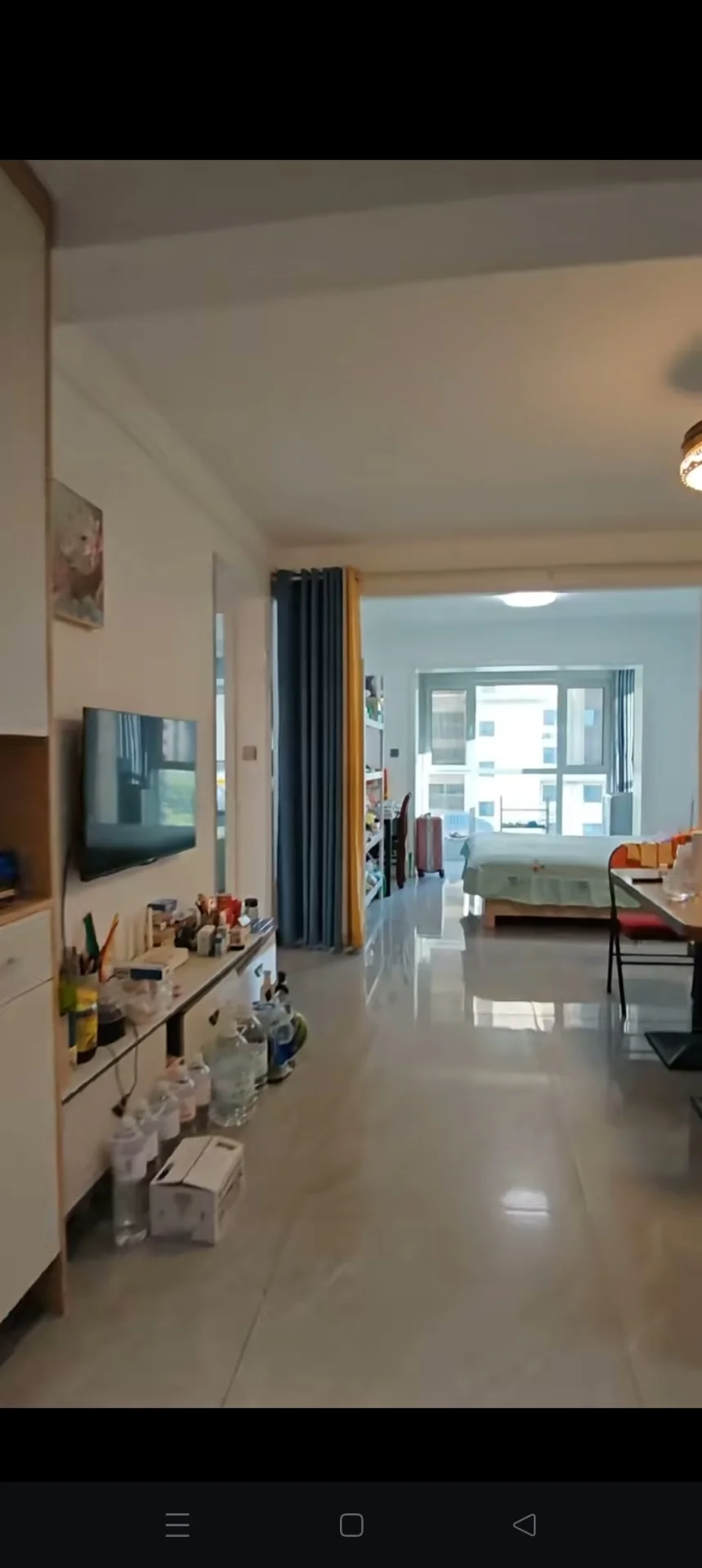 这是一个宽敞的室内空间，地面采用浅色大理石材质。空间内摆放着电视和一些展示物品，整体装修风格偏向实用和现代简约。采光良好，营造出明亮、开阔的氛围。