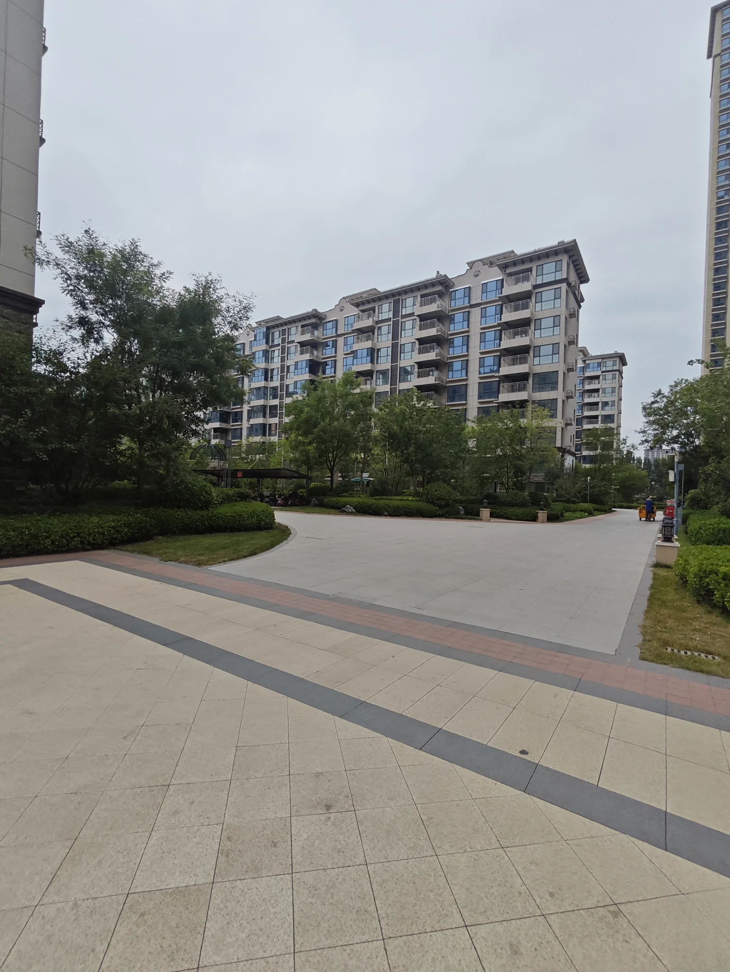 多栋现代风格的高层住宅建筑群，外立面以浅色调为主，配有整齐的绿化带和社区道路，整体呈现出一种现代、有序的城市居住氛围。