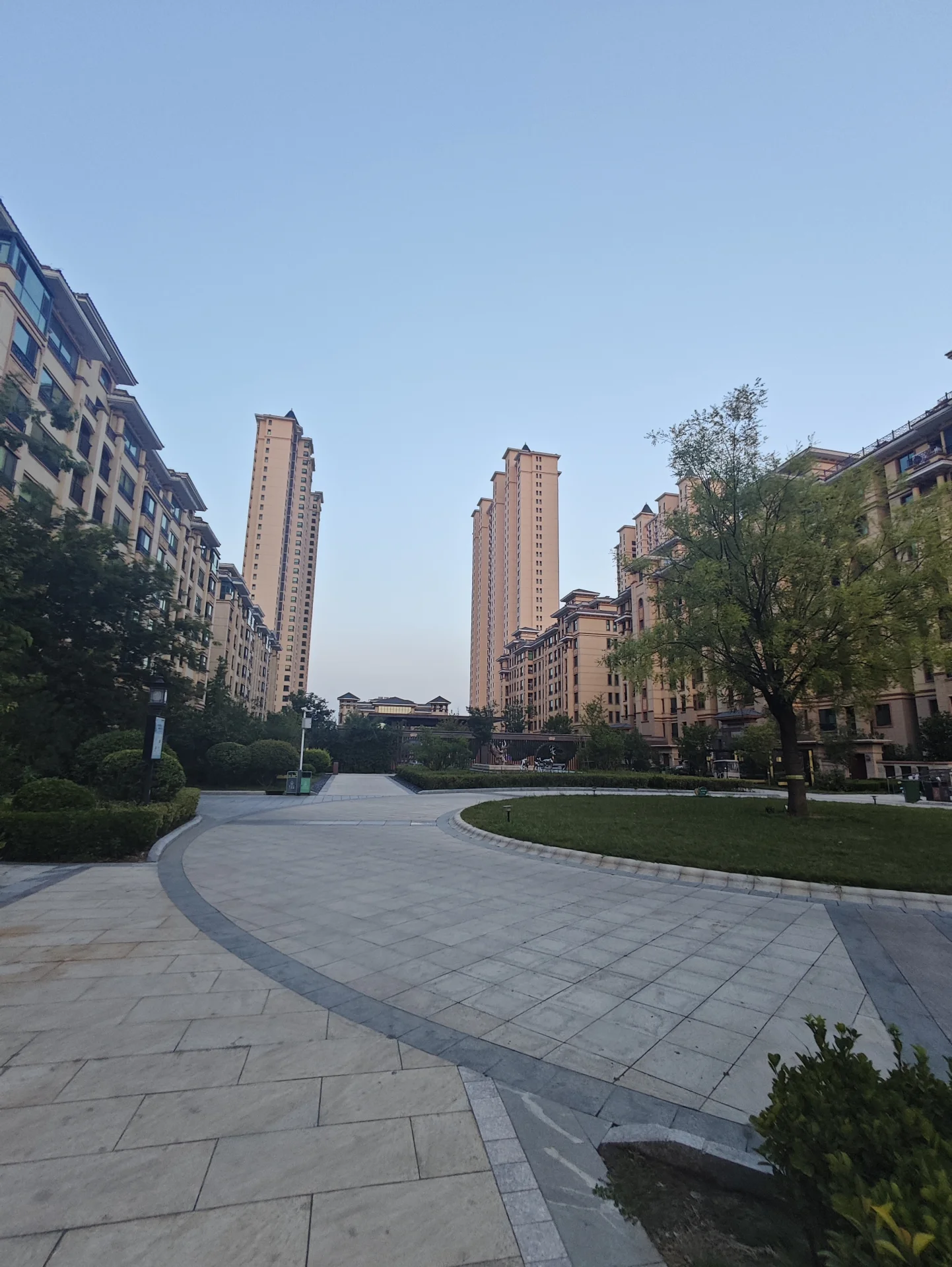 多栋高层住宅建筑群的立面清晰可见，建筑风格统一，周围环绕着修剪整齐的绿化带和铺设平整的广场，整体呈现出城市居住区宁静而有序的氛围。