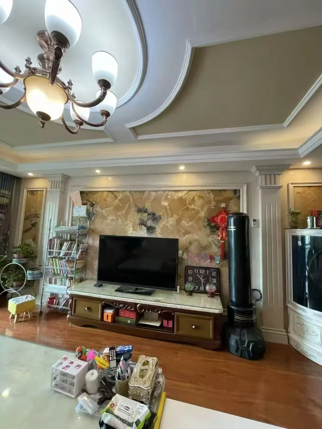 客厅场景，墙面采用暖色调，配有大型平板电视和古典风格的吊灯。采光良好，整体呈现温馨、略带复古的居家氛围。