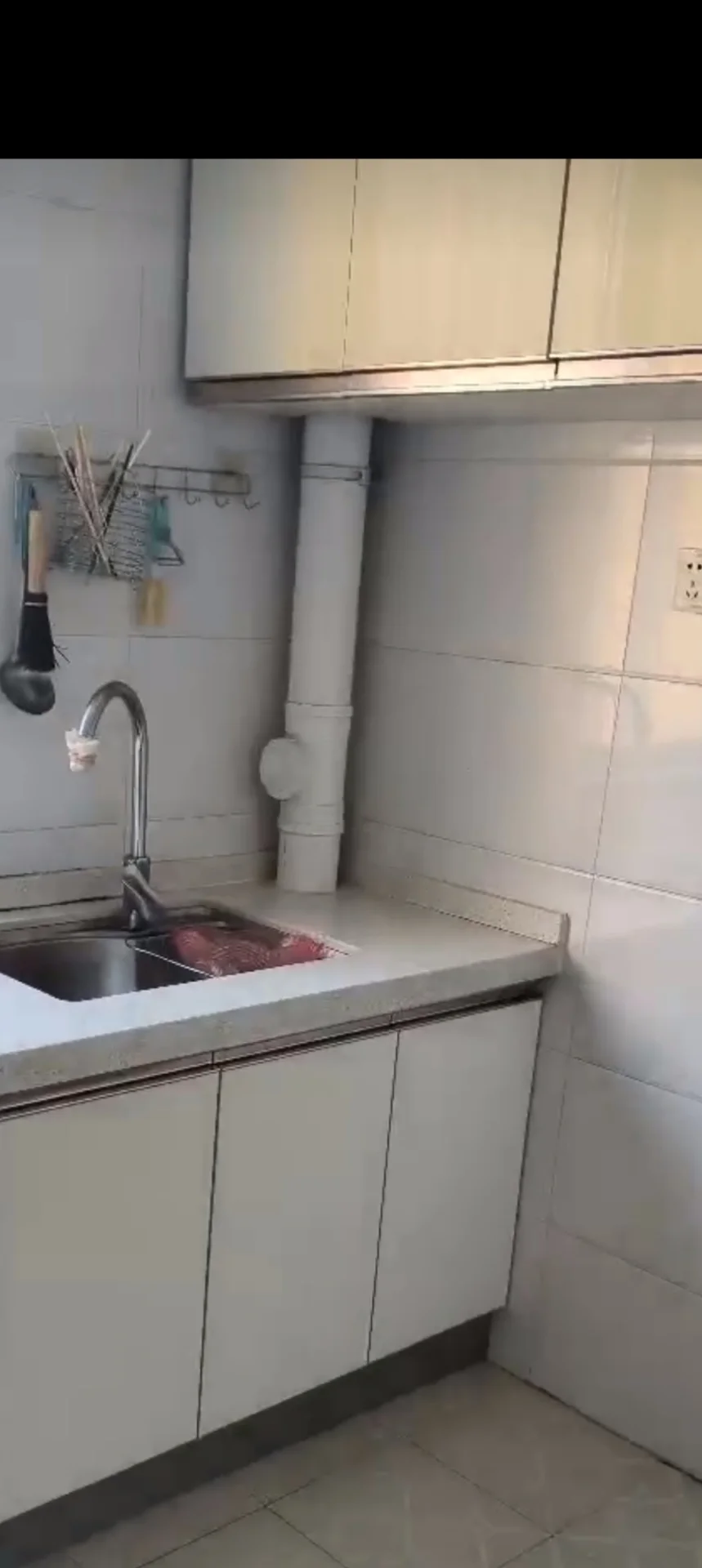 厨房空间，采用白色橱柜和浅色台面设计，地面铺设米色瓷砖，配有水槽和吊柜。光线明亮，整体呈现简洁、实用且整洁的现代厨房装修风格。