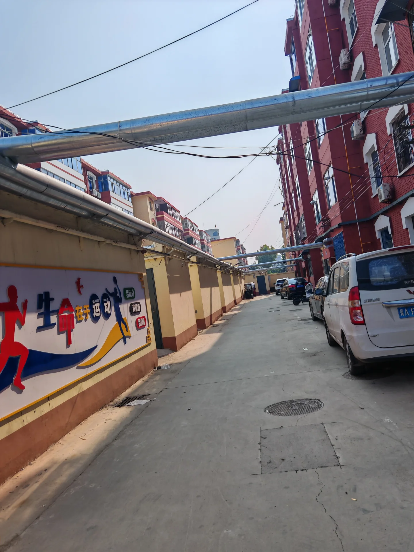 一条城市街道的景象，两侧是多层住宅建筑，建筑立面以红砖为主，街道上有车辆停放，整体呈现典型的城市居住环境氛围。