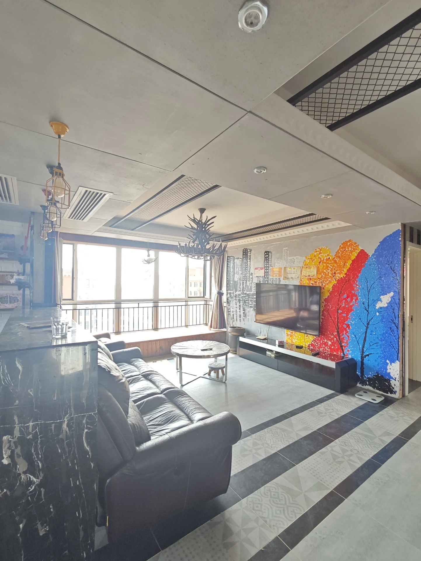 客厅场景，墙面采用现代简约风格，配有深色沙发和大型平板电视。采光良好，整体呈现现代舒适的居住氛围。