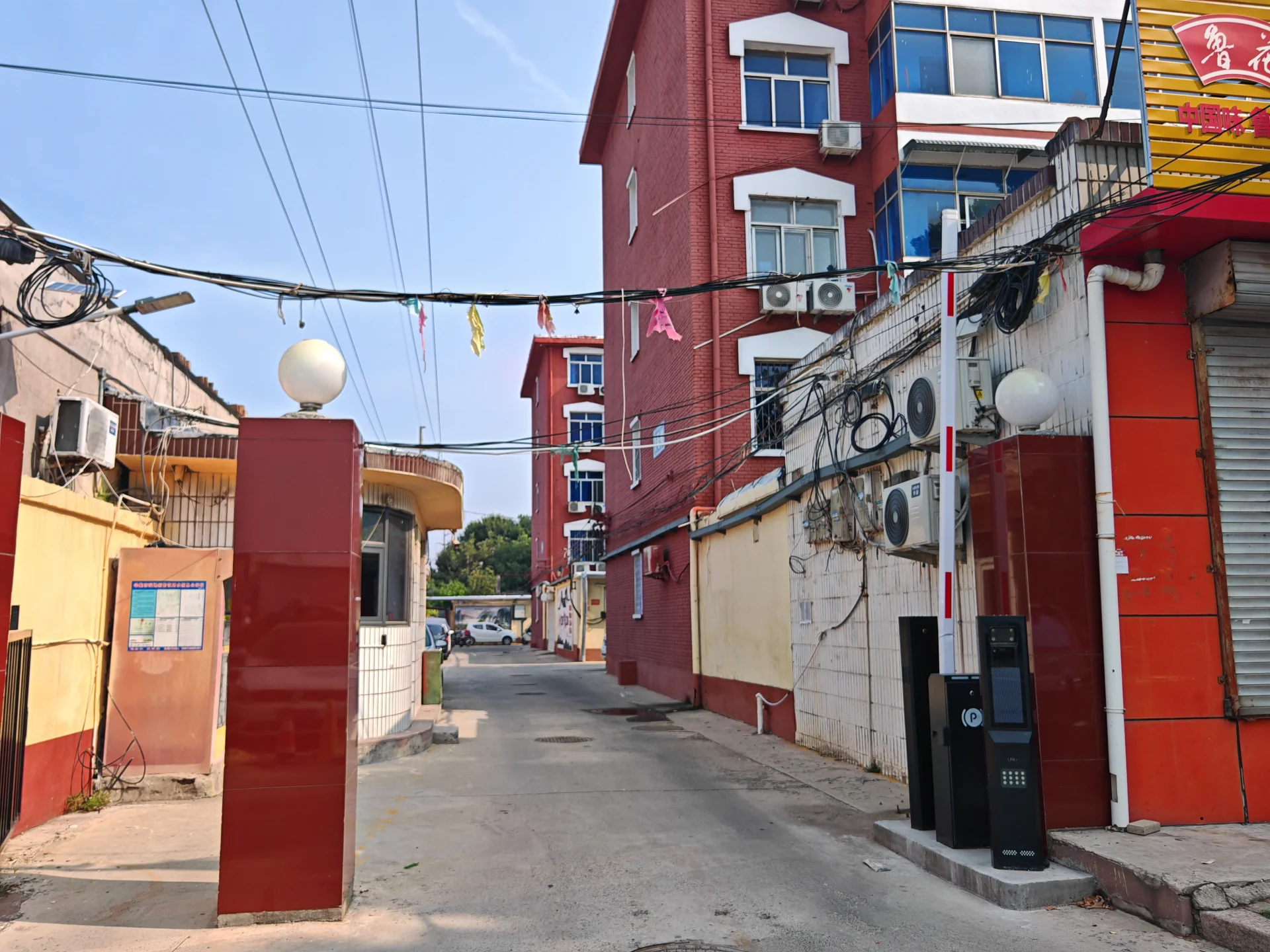 一排多层住宅建筑的外部立面，建筑外墙呈现红白相间的色彩，街道上有电线和外部空调外机等设施，整体展现了社区或城市街道的居住环境氛围。