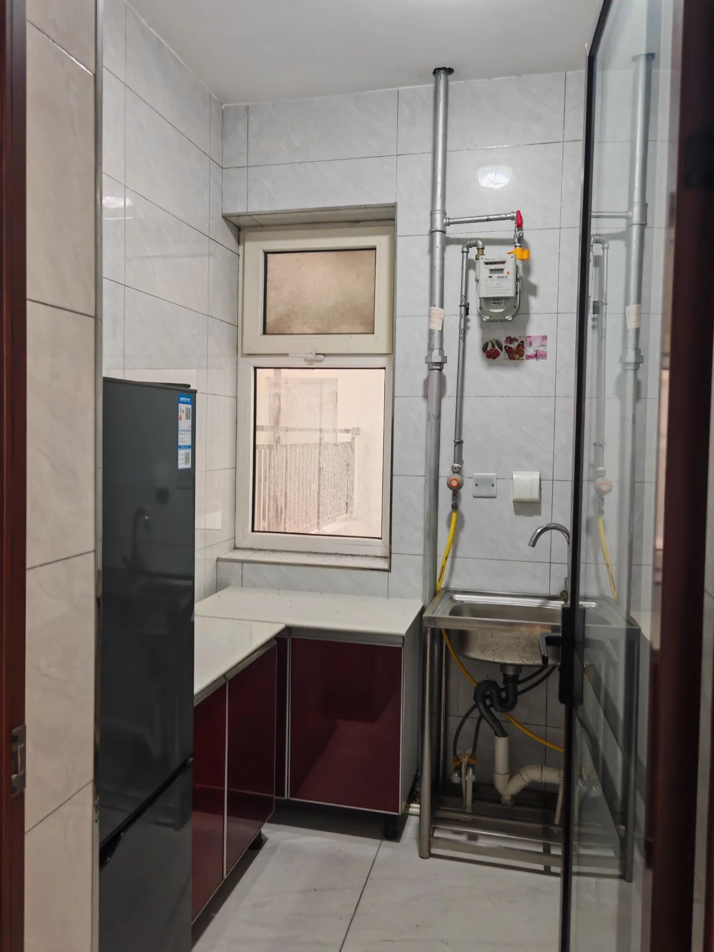 一个浴室空间，地面铺设米色瓷砖，墙面为白色瓷砖，配有淋浴设施和管道系统。空间光线明亮，整体呈现功能性强、卫浴设施齐全的现代简约装修风格。