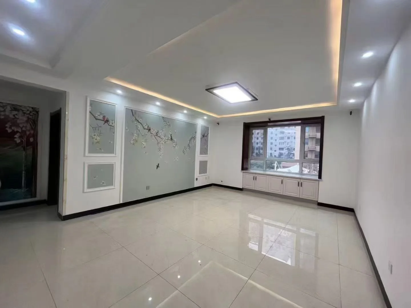 一个宽敞的室内空间，地面铺设大面积浅色瓷砖，天花板采用嵌入式筒灯照明，墙面装饰有简约的装饰线条，整体呈现出明亮、整洁的现代简约装修风格。