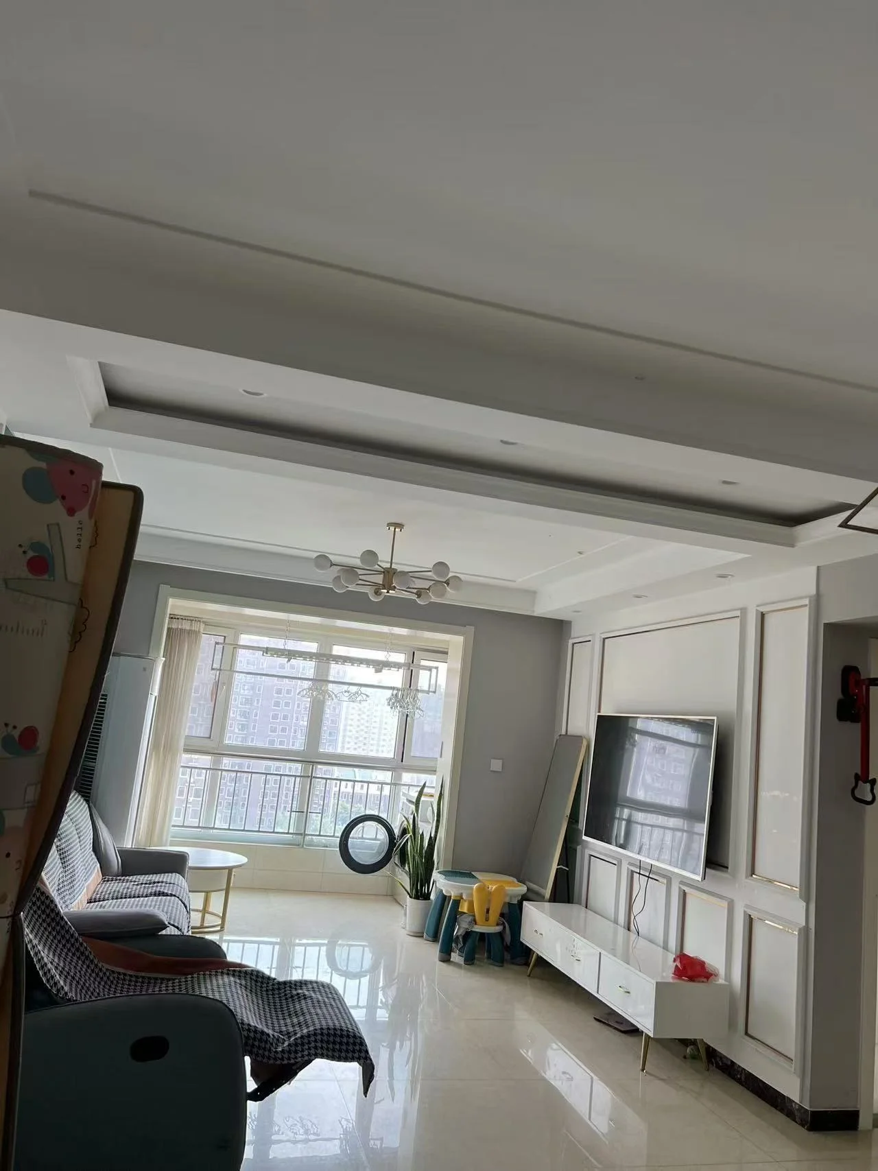 现代简约风格的住宅内部空间，地面铺设大理石或大理石纹瓷砖，采光良好，配有现代简约风格的家具和大型平板电视。整体空间布局整洁舒适，呈现出温馨的居住氛围。