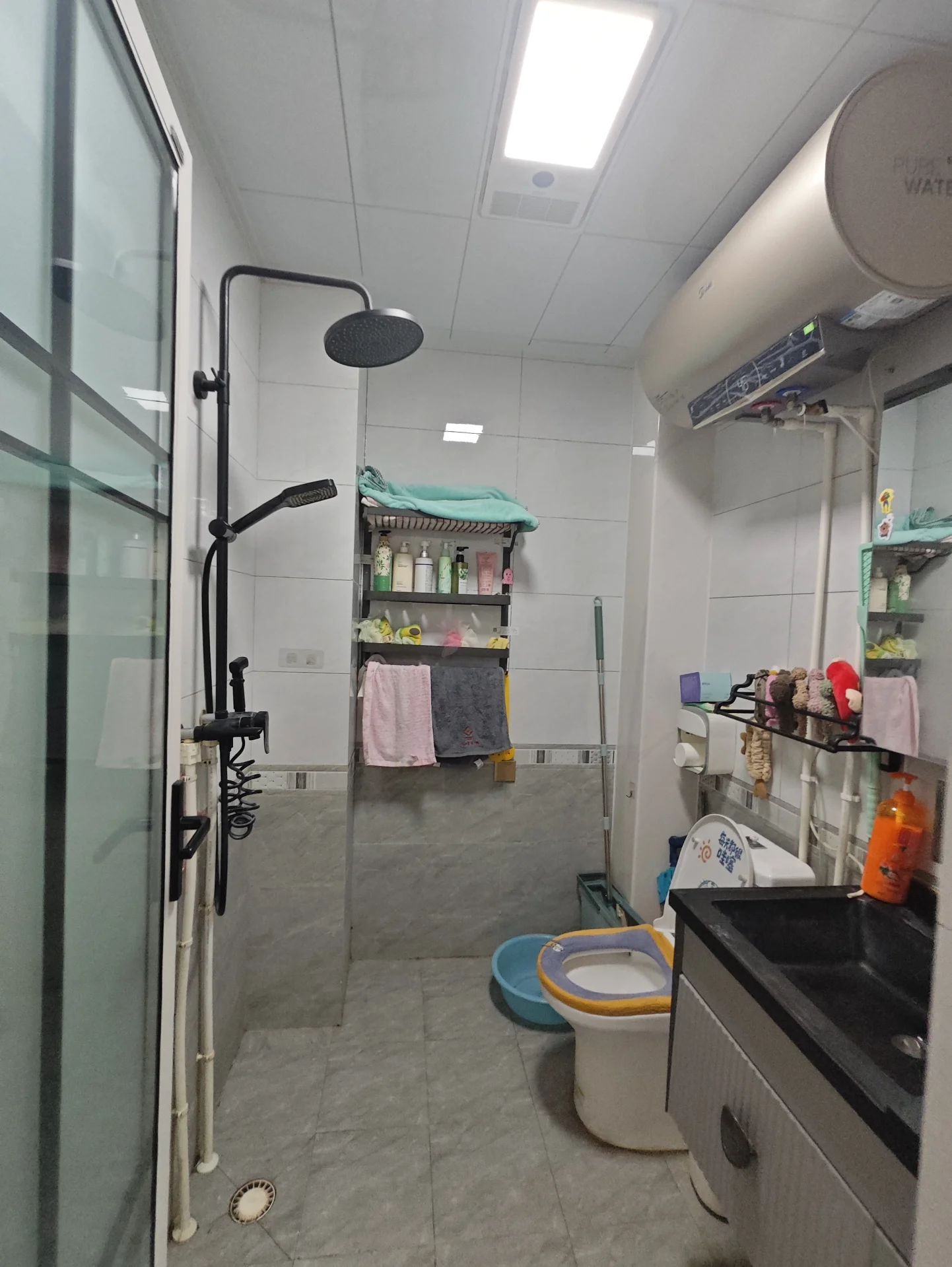 一个室内卫生间或储物间场景，地面铺设米色瓷砖，配有洗手台、储物柜和简易的储物架。光线明亮，整体环境功能性强，呈现基础的实用性空间。