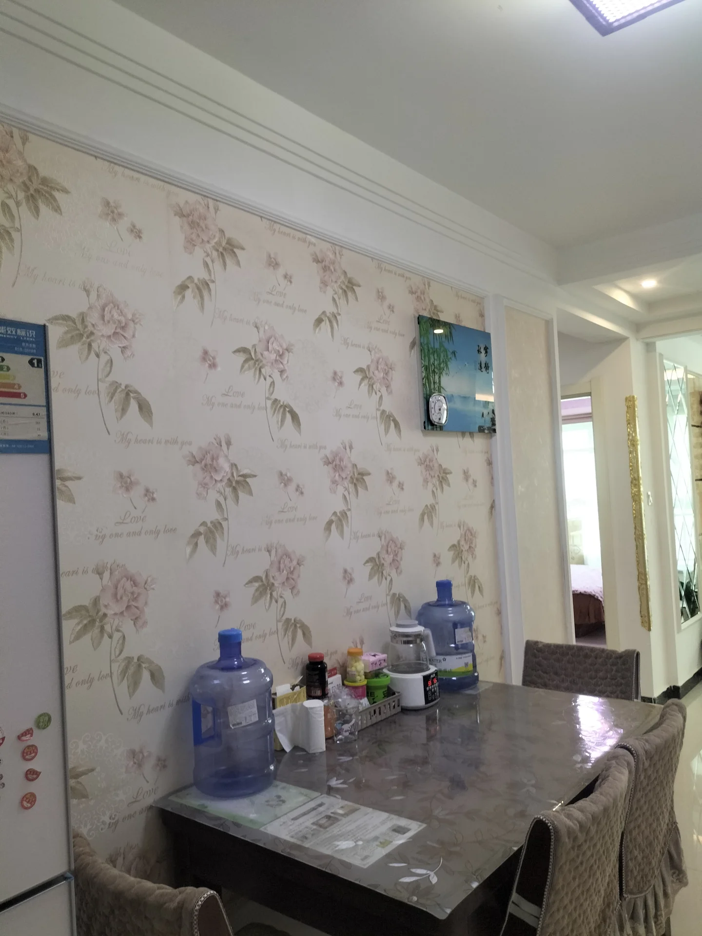 一个室内环境图，墙面铺设了带有粉色花卉图案的墙纸，地面铺设了深色大理石纹理的地面。空间内摆放着几台水瓶和一些小物件，整体呈现一种温馨、略带复古的居家氛围。