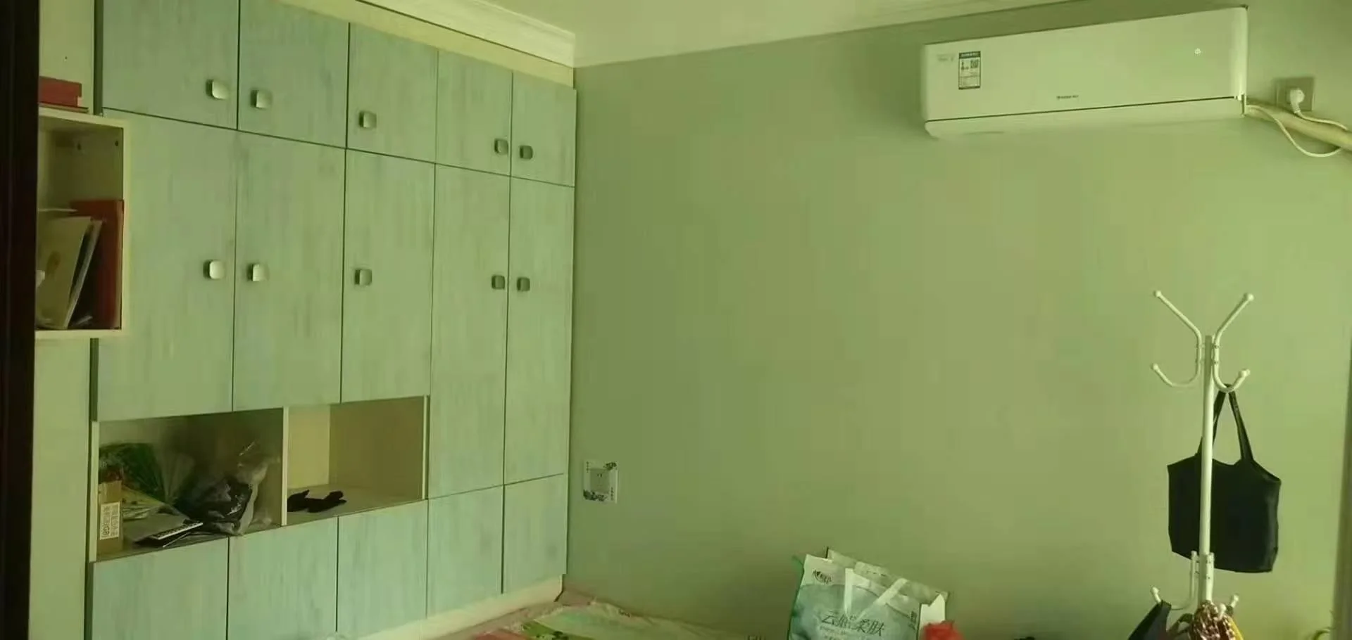 厨房或储物空间场景，墙面为浅绿色，配有大量浅色木质橱柜。空间光线适中，安装有空调，整体呈现功能性强、简洁的储物氛围。