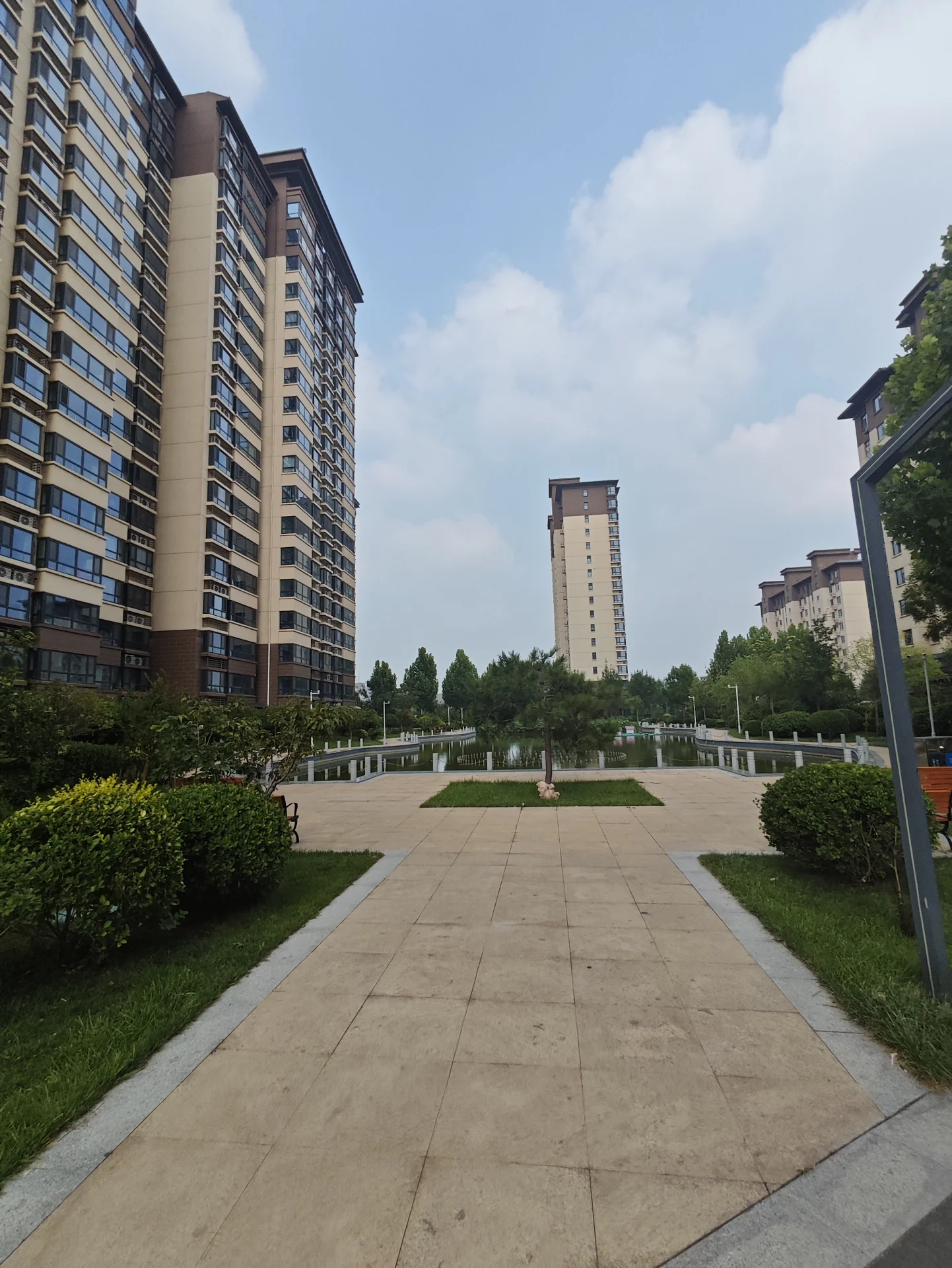 多栋现代高层住宅的外部立面清晰可见，建筑立面以玻璃和混凝土为主，周围环绕着修剪整齐的绿化带和公共广场，整体呈现出一种现代、有序的社区居住氛围。