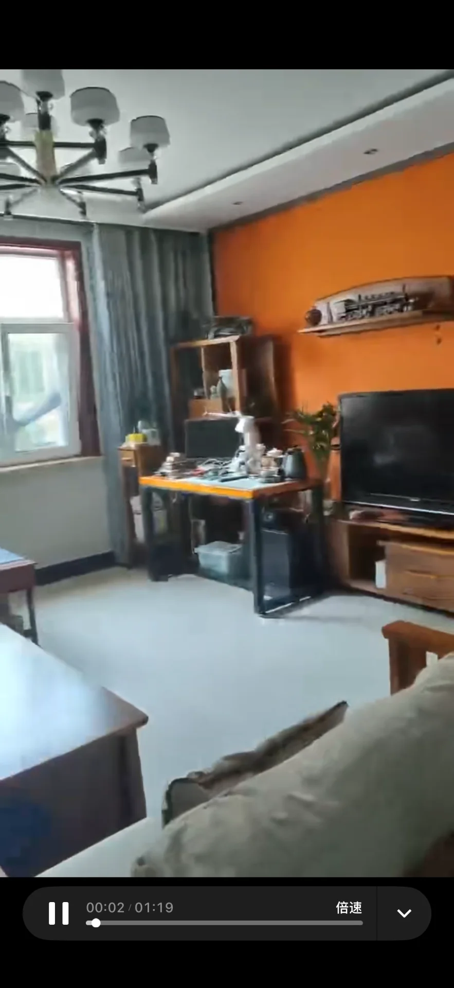 客厅场景，墙面采用橙色调，配有大型平板电视和沙发。采光良好，整体呈现现代简约装修风格，氛围整洁舒适。