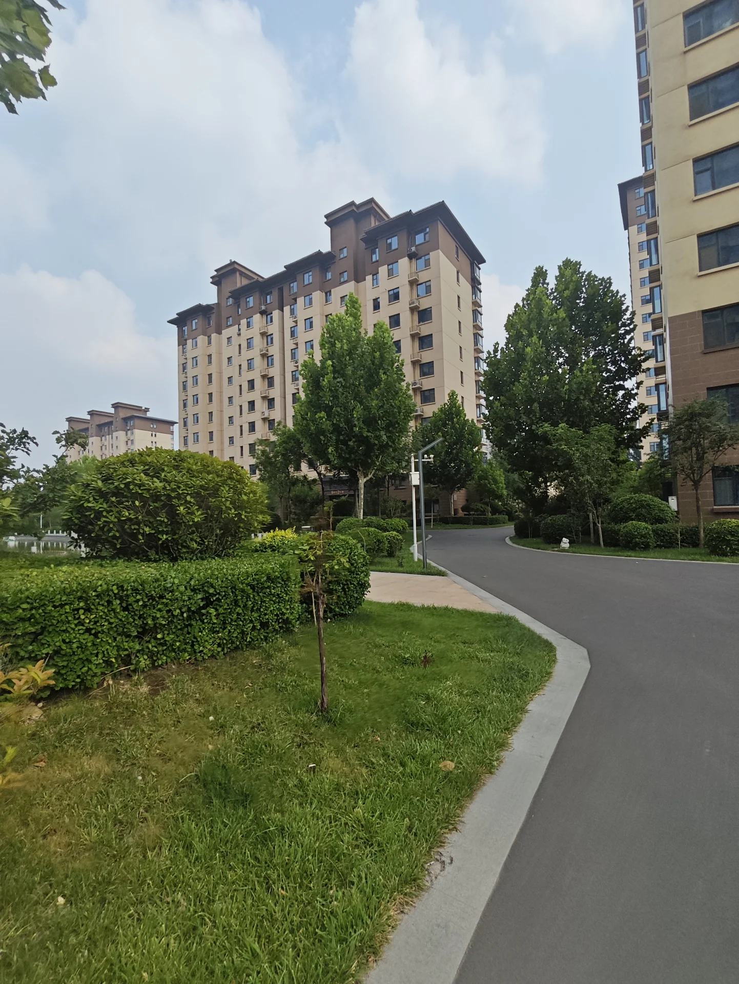 一栋多层住宅楼的外部立面清晰可见，建筑风格较为现代，周围环绕着修剪整齐的绿化带和树木，整体呈现出社区环境整洁、宁静和谐的居住氛围。