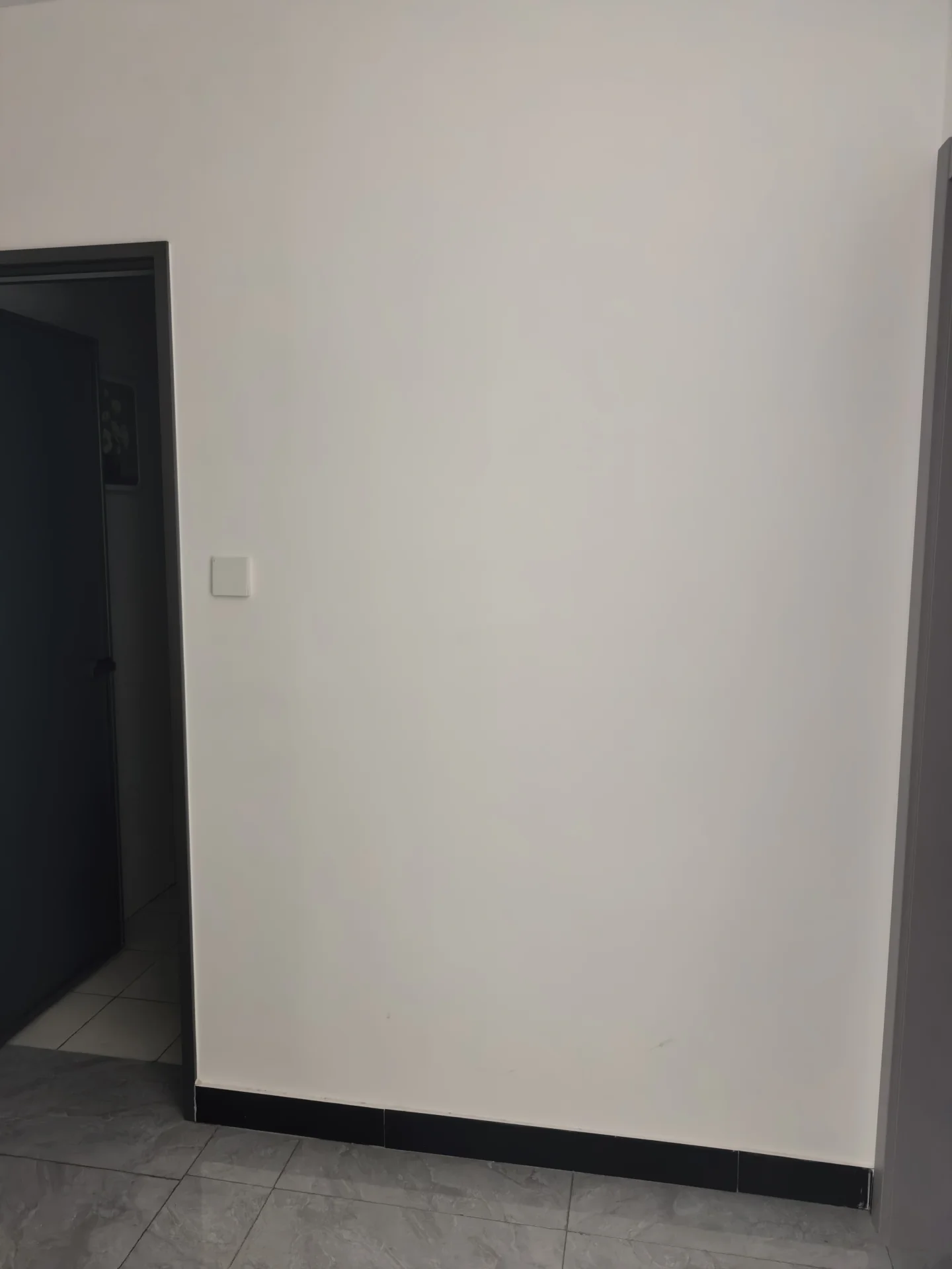 一个极简的室内空间，墙面为纯白色，地面铺设深色地砖，光线均匀，整体呈现出干净、空旷的现代简约装修风格。