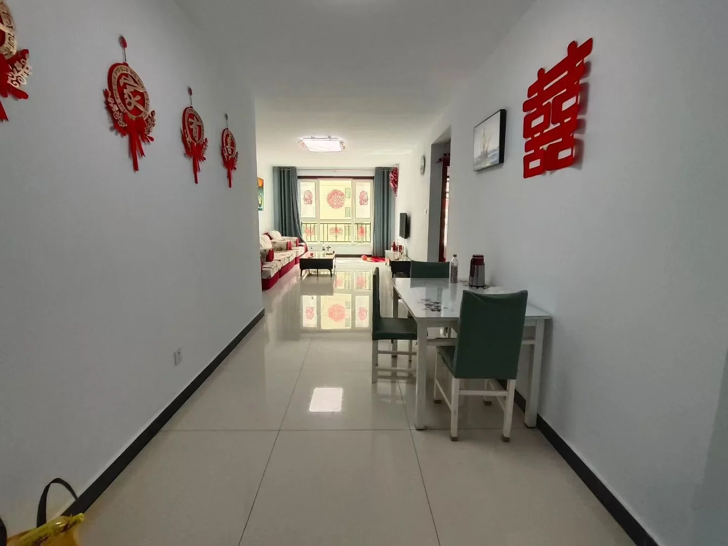 一个走廊或大厅场景，墙面装饰有红色的传统图案，地面铺设米色瓷砖，光线明亮，整体呈现简洁的居住环境氛围。