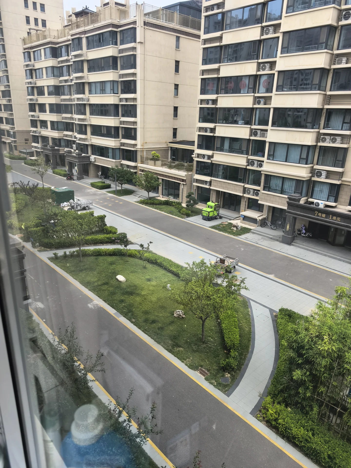 多栋现代风格的住宅楼外立面，外墙以浅色调为主，配有规则的窗户。建筑前方有精心设计的街道绿化带和低矮的植被，整体呈现出一种有序、宁静的城市社区氛围。