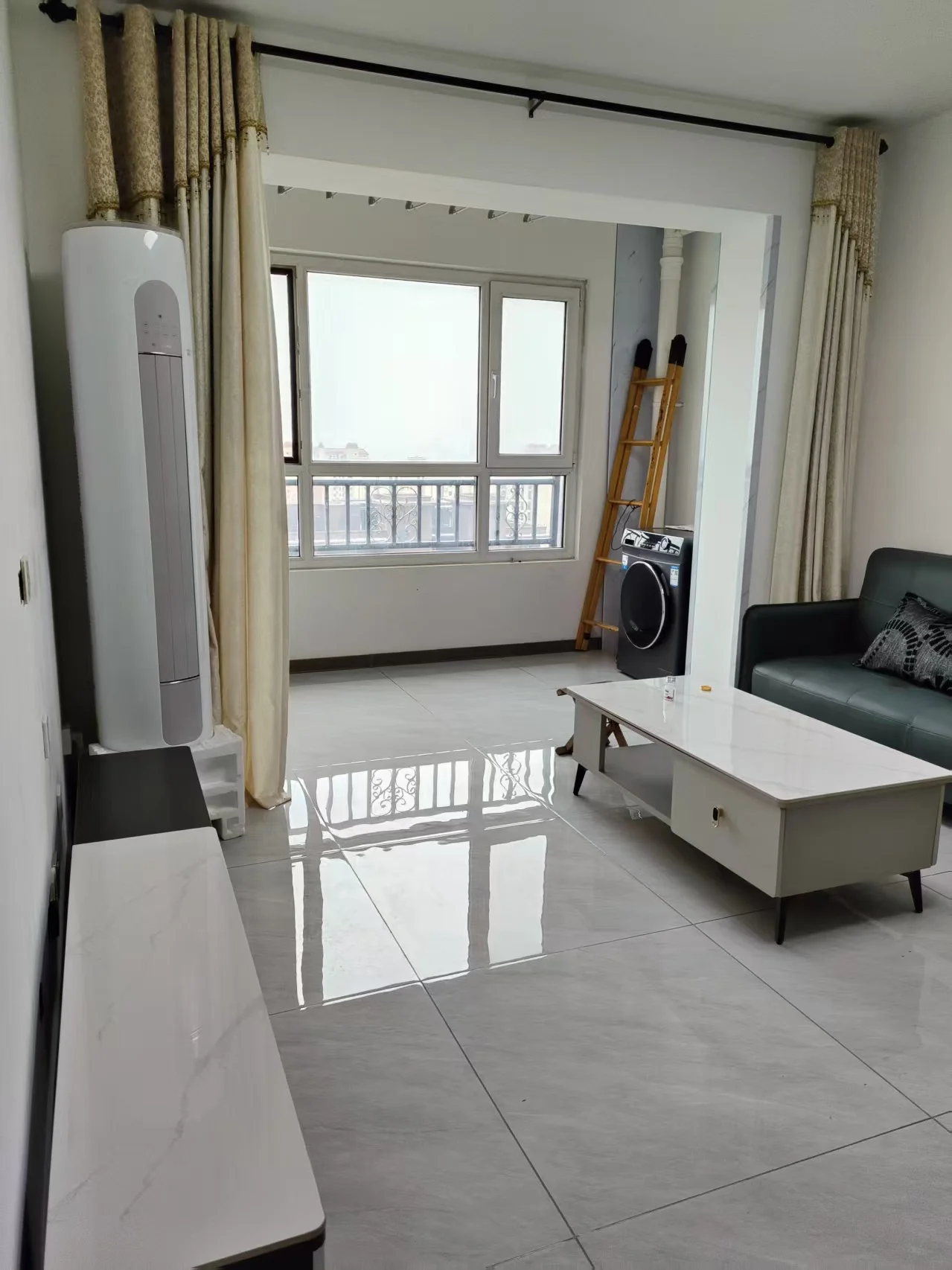 现代简约风格的室内居住空间，地面铺设浅色瓷砖，配有现代简约风格的沙发和电视柜。采光充足，整体环境整洁舒适，呈现出温馨的居住氛围。