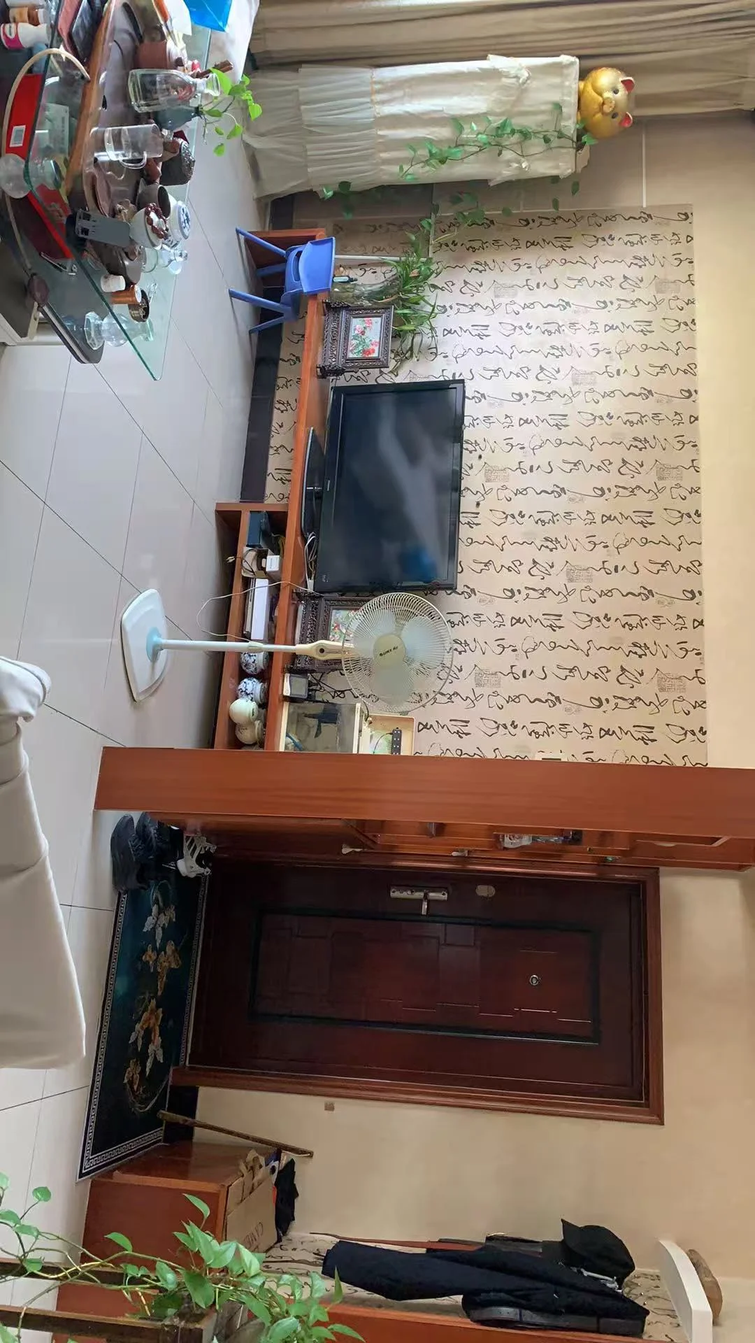 一个室内空间，装修风格以木质色调为主，配有大型平板电视、多层储物架和各种装饰物。空间光线适中，整体呈现温馨、实用且略显杂乱的居住或商业内部氛围。