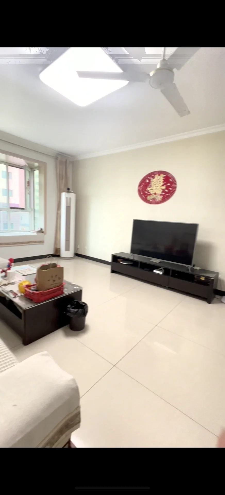 卧室场景，地面铺设白色瓷砖，配有床铺、电视柜和吊扇等家具。采光良好，整体呈现简洁明亮的现代简约装修风格，氛围整洁舒适。