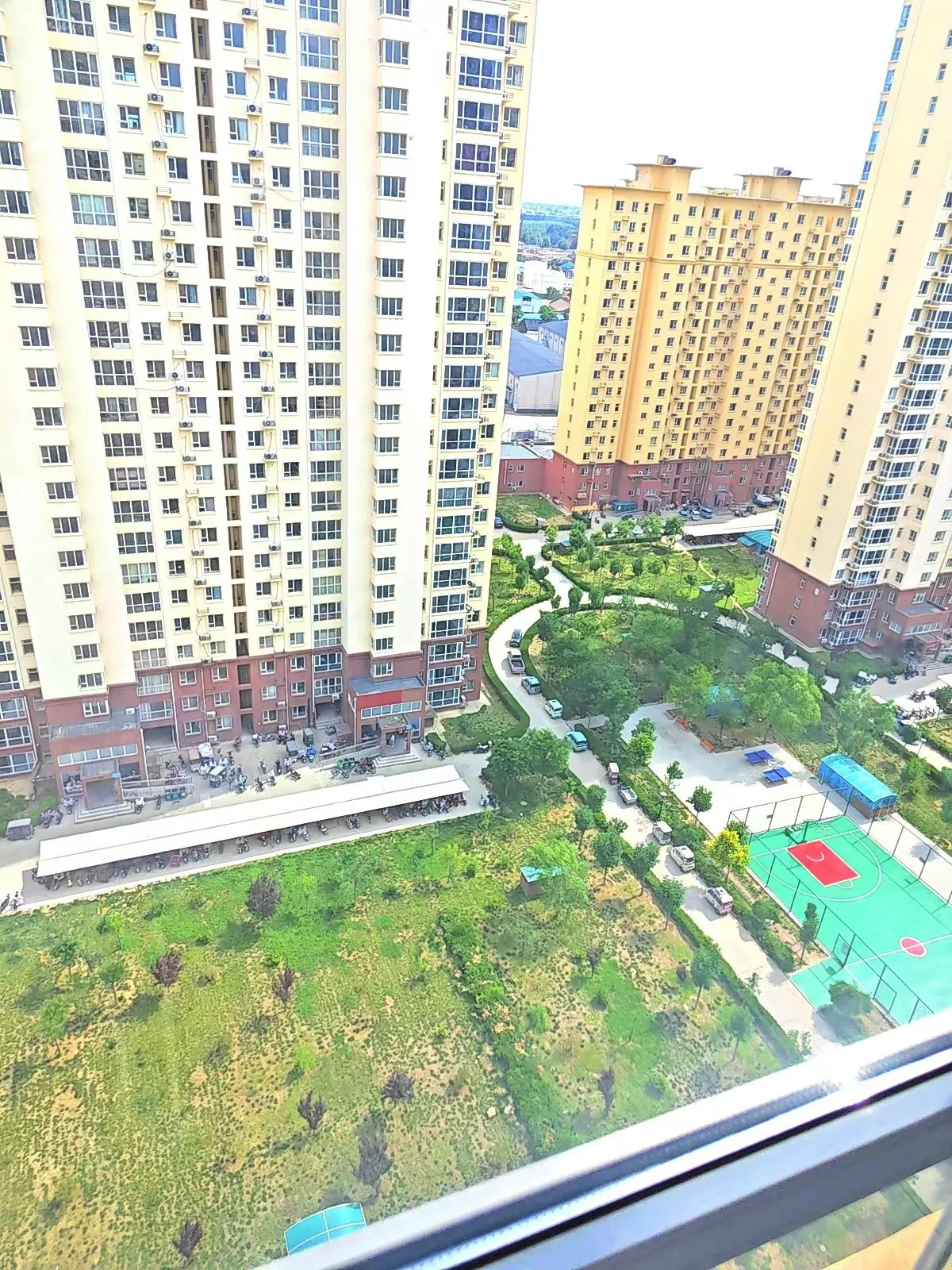 城市绿地，有网球场和游泳池，周围高楼林立，有车辆和人在附近活动。