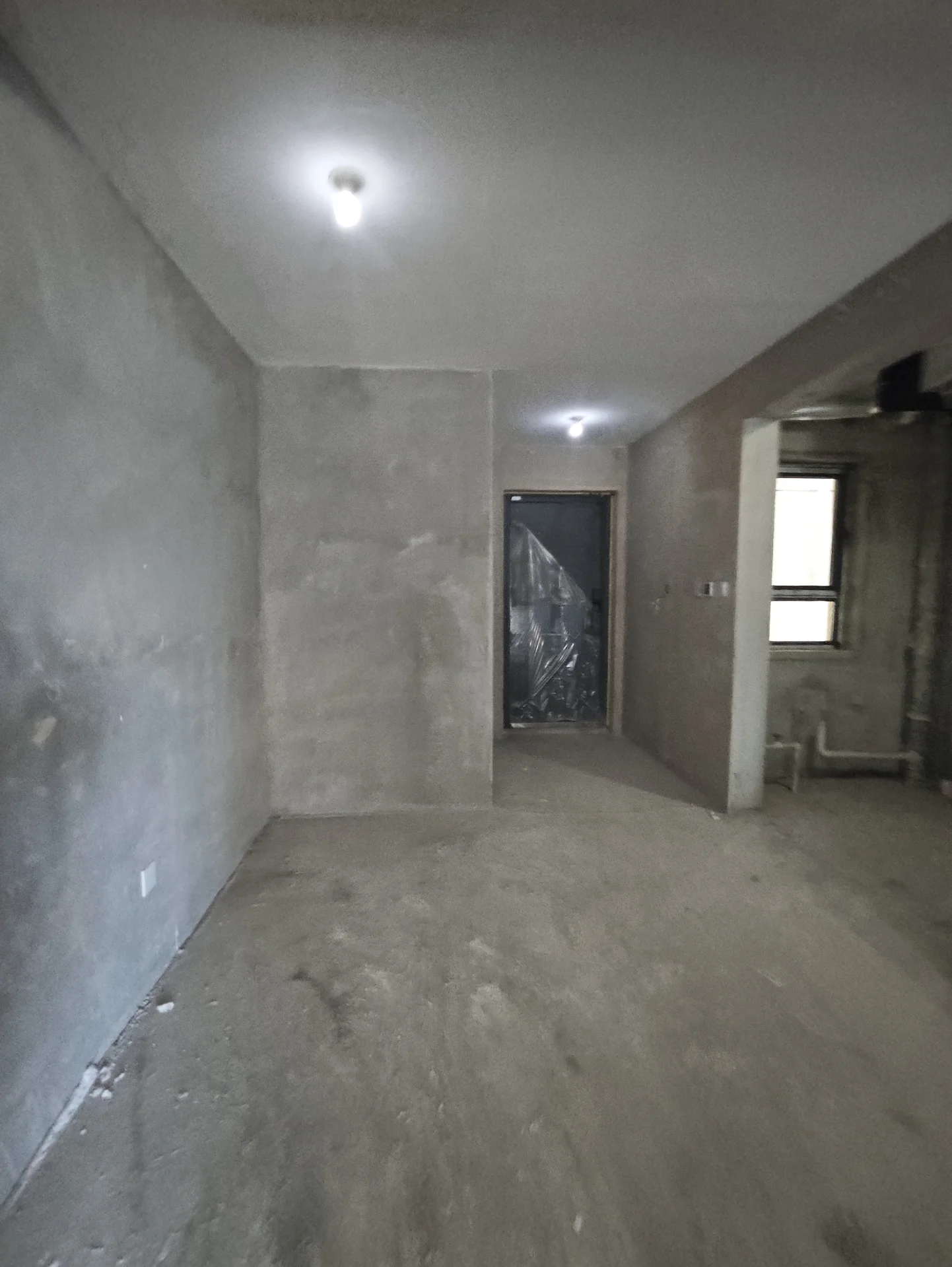 空旷房间，地面和墙壁为混凝土材质，有门和窗户。房间处于施工或翻新阶段，目前为空置状态，无家具和其他物品。氛围表明房间正在改造或完成中。