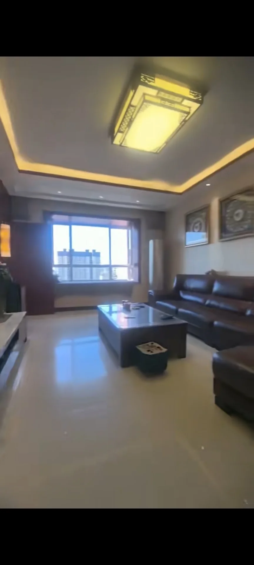住宅客厅，棕色沙发居中，茶几置于沙发前，电视位于左侧，天花板悬挂灯饰照明。