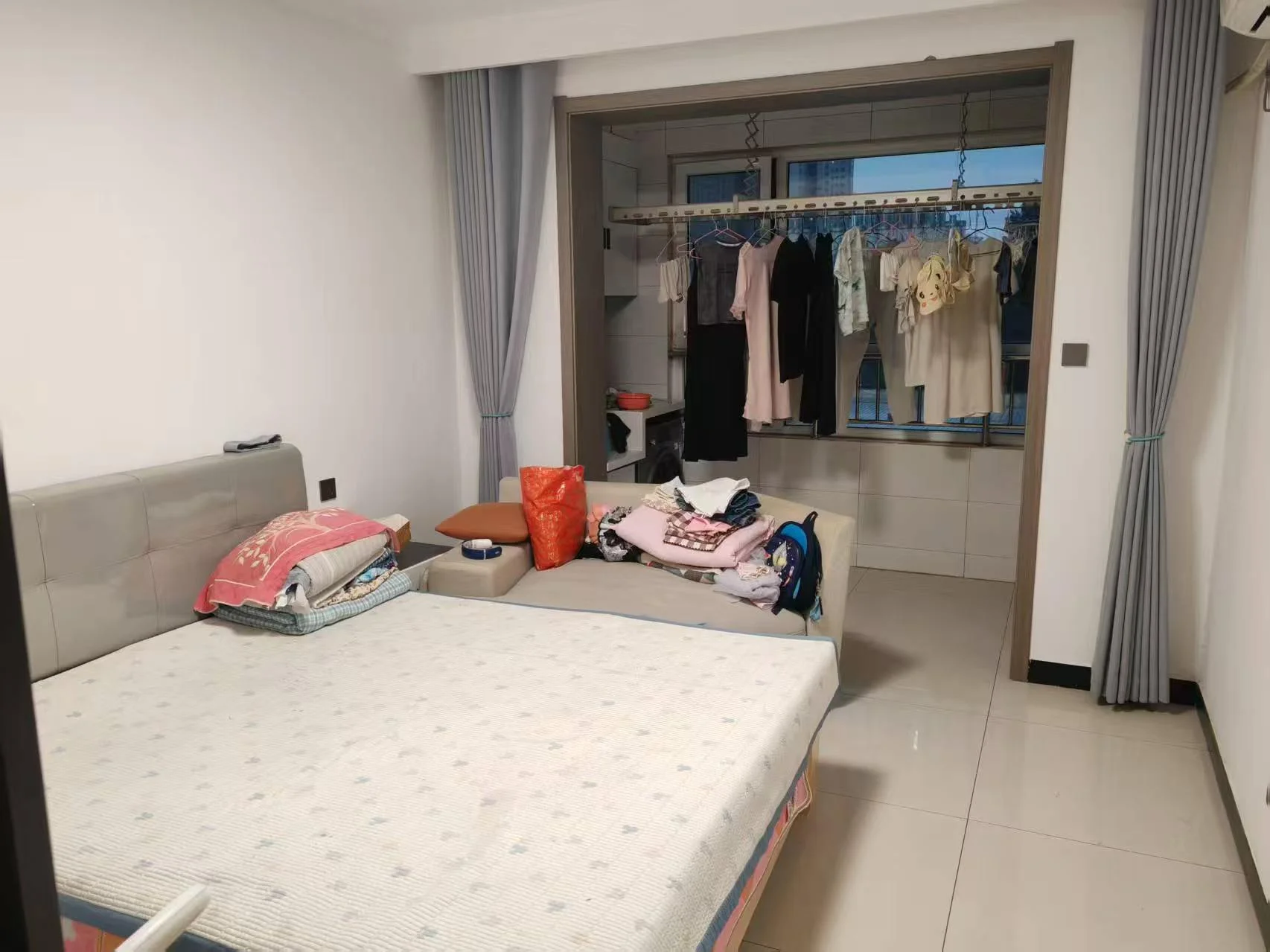卧室，白色调，整洁明亮，有衣物晾晒，家具整齐排列，窗户和门暗示是更大空间的一部分。