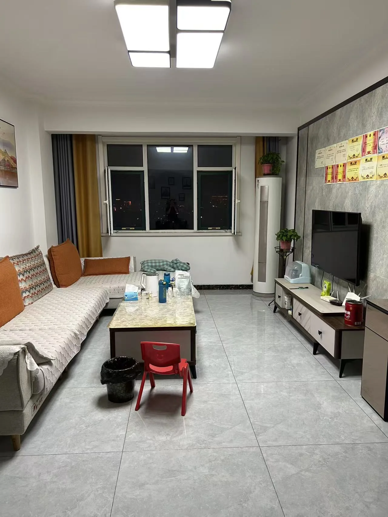 宽敞客厅，灰色地砖、白色墙面和大窗户，配有沙发、茶几和电视，屋内还有一把椅子。氛围宁静宜人，家具和空间布局是重点。