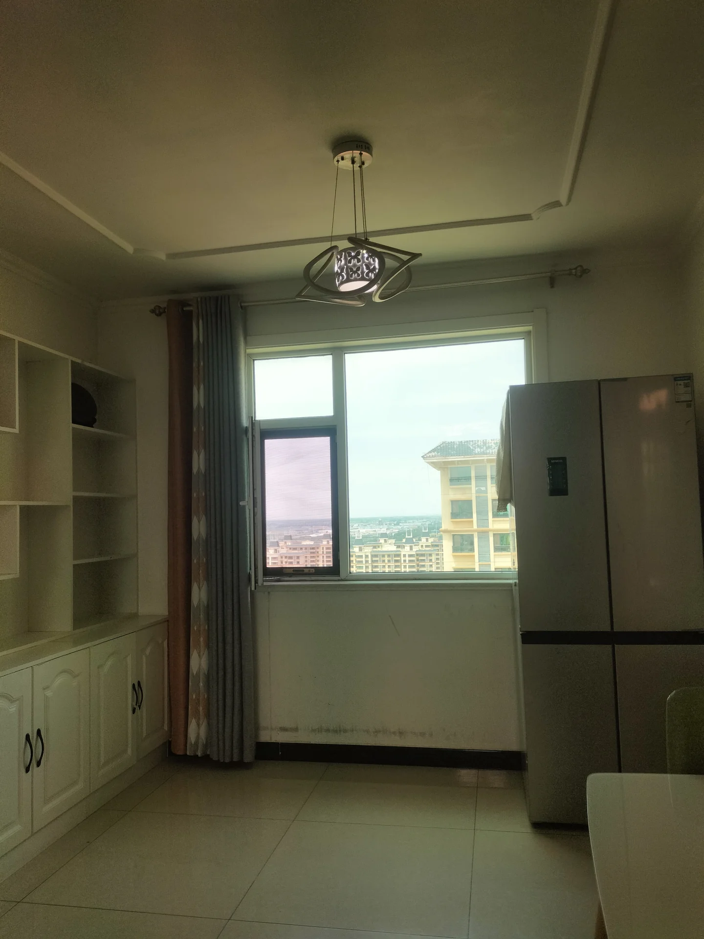 空房间，白色墙壁和地板，家具有餐桌和椅子，装饰简约，氛围略显阴沉，窗户暗示可能有自然光。