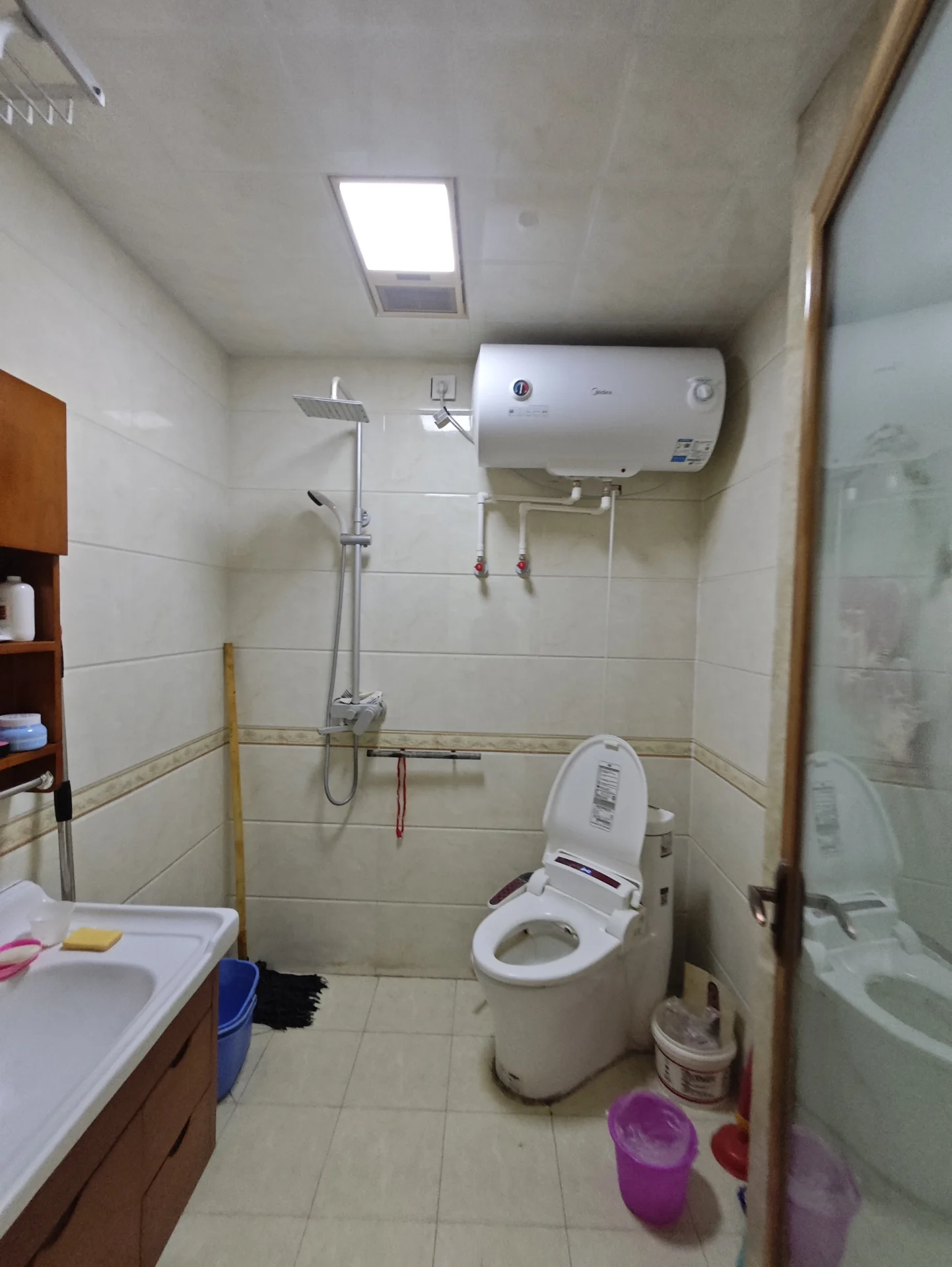 浴室，墙壁和地板铺设瓷砖，颜色以米色或浅棕色为主，氛围功能性强但略显简陋，光线充足。