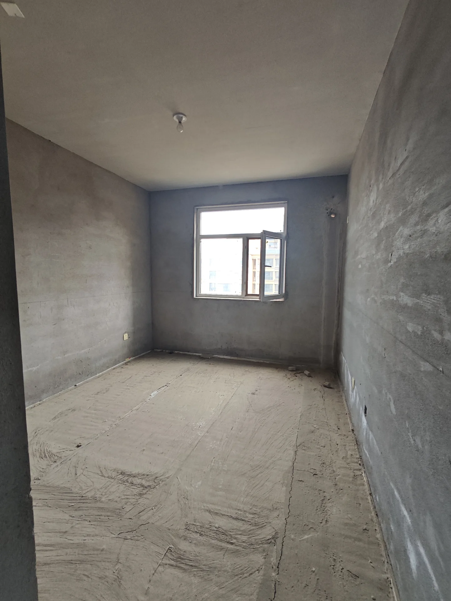 空旷施工房间，墙面和地面未完成，裸露的混凝土墙面和尘土覆盖的地板，房间内无装饰或家具，氛围显得正在改造或完成中。