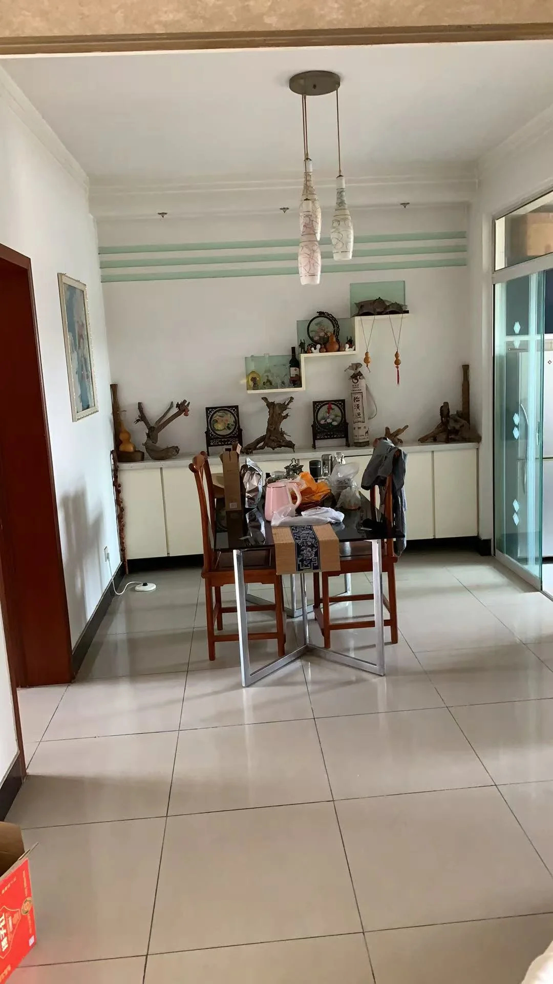 一个宽敞的室内空间，地面铺设米色瓷砖，墙面采用浅色调，配有木质或浅色系家具。空间内悬挂着吊灯，整体呈现温馨、朴素的居住氛围。