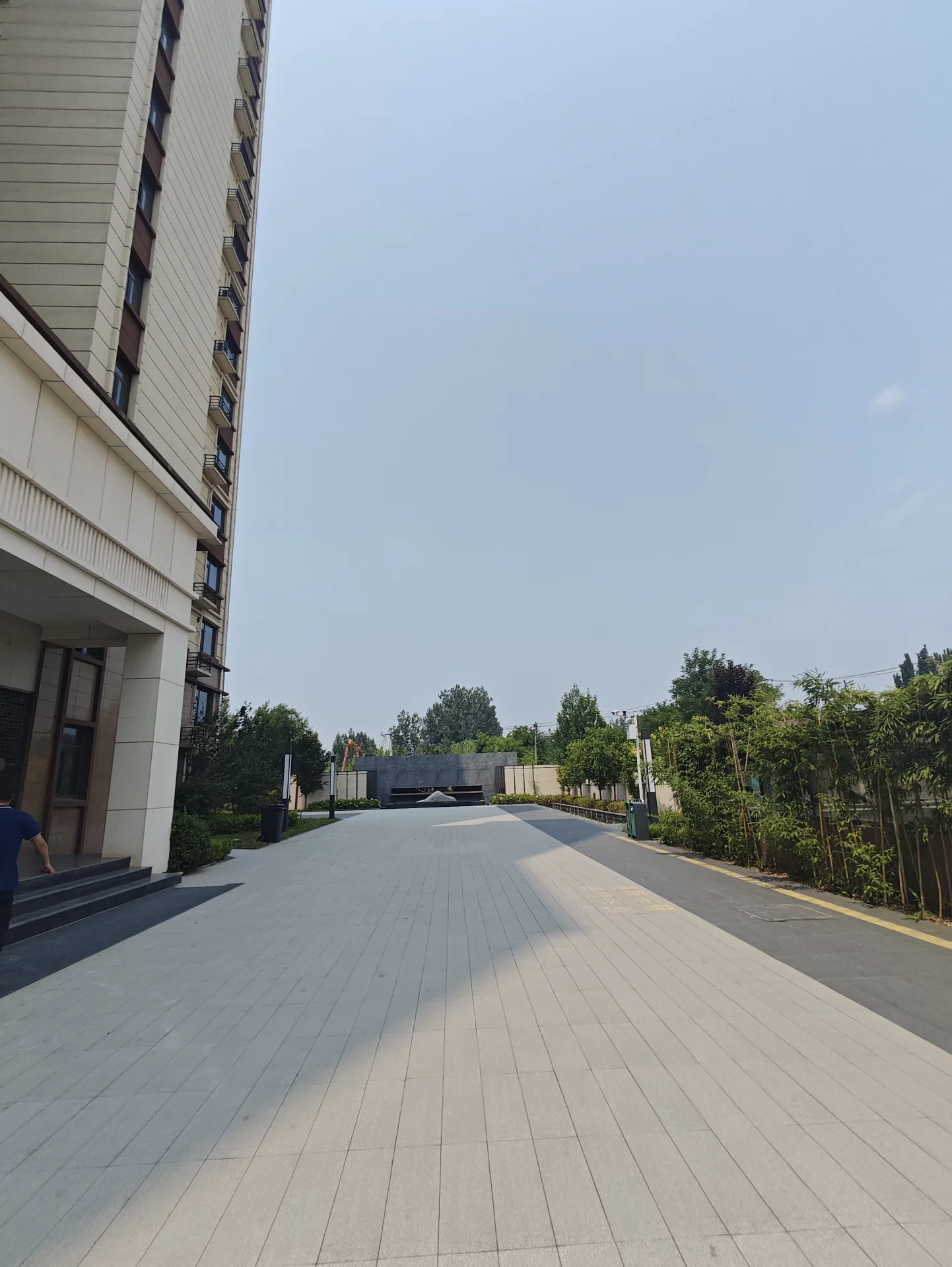 白色大楼，前有空旷停车场，无人员活动。建筑似高层公寓，天空晴朗蔚蓝，氛围宁静安静。