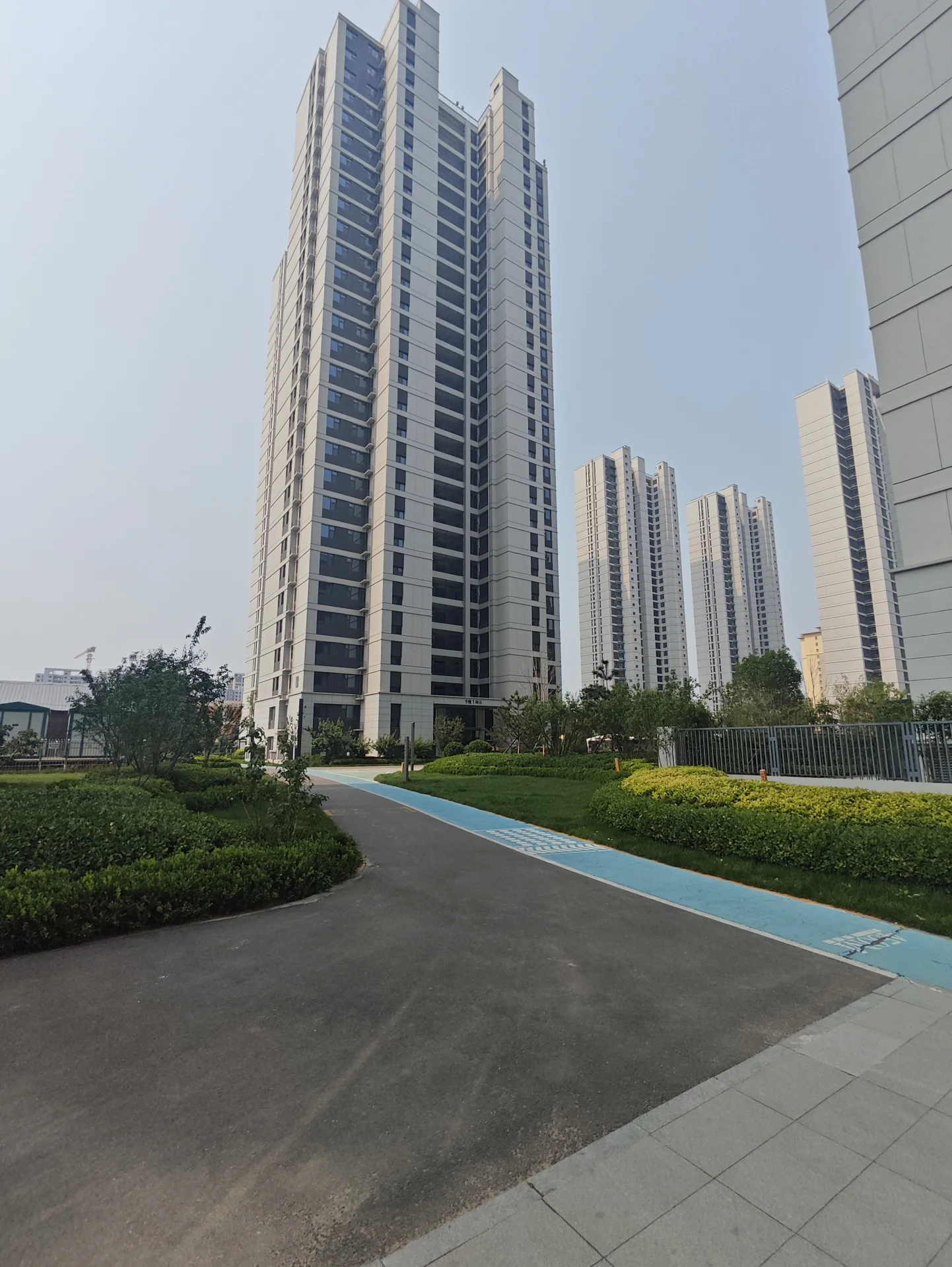 现代大楼，有长窄的车道通往建筑，周围是其他高楼大厦，场景位于城市区域或商业区，建筑外观引人注目。车道是主要特征。
