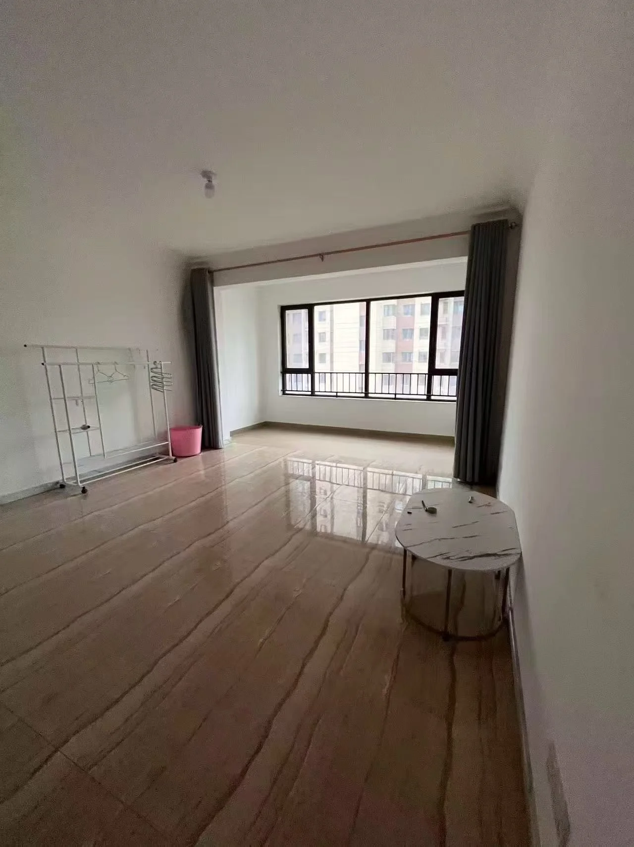 空旷房间，木地板和白色墙壁，有桌子和椅子等家具，角落里有一只粉色垃圾桶，整体简洁 minimalist。