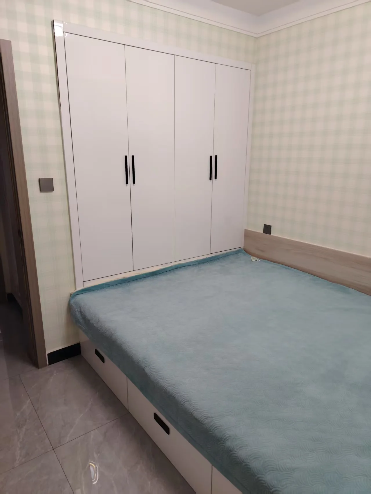 卧室空间，墙面采用米色格纹墙纸，配有大面积的白色衣柜和床铺。采光良好，整体呈现简洁整洁的居住氛围。