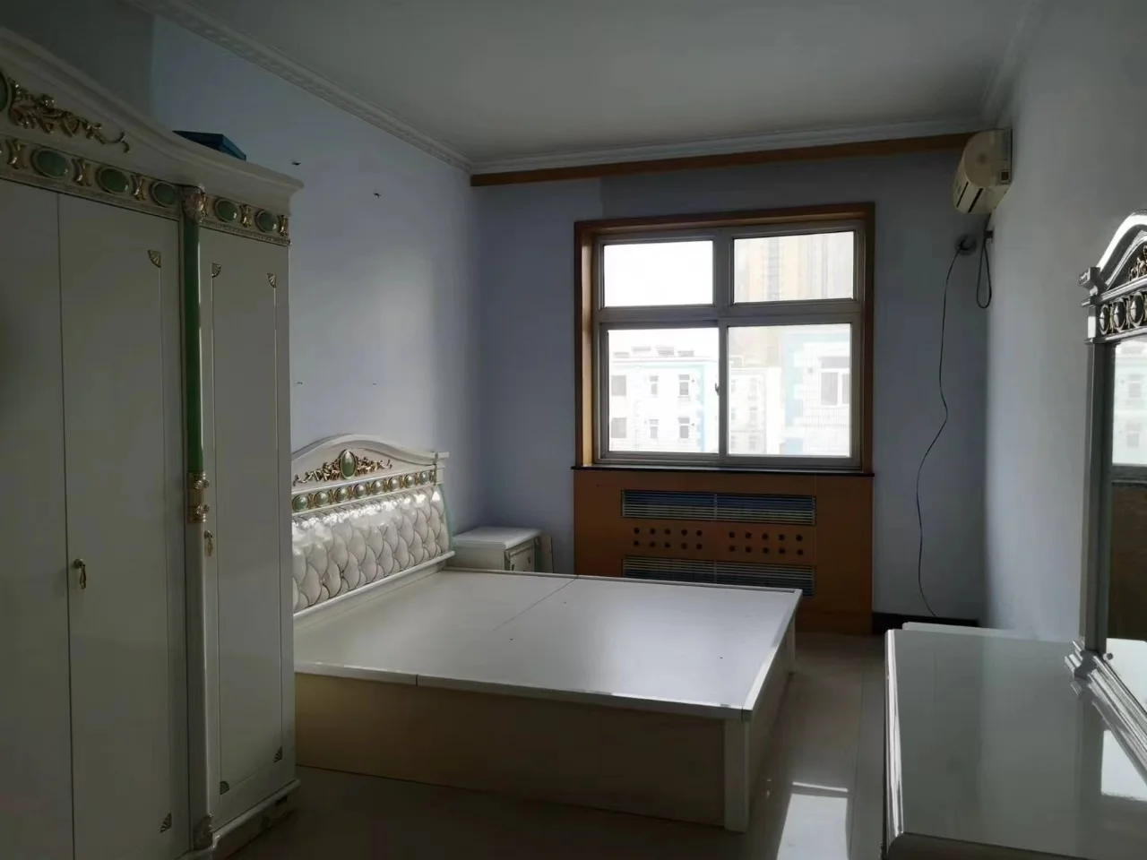 卧室场景，墙面为柔和的蓝色，配有大尺寸衣柜和床铺。采光良好，整体呈现简洁、温馨的居住氛围。
