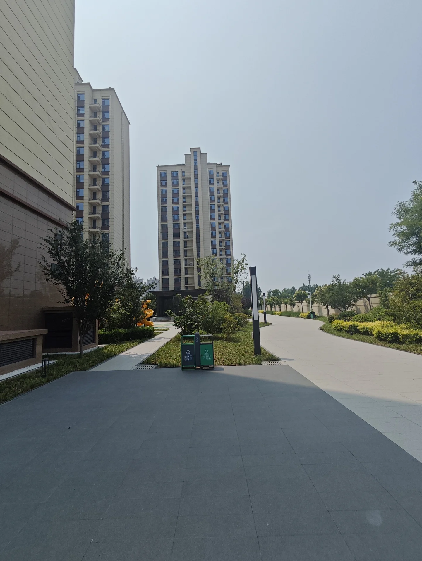 开阔庭院，有步行道穿过，周围是高大建筑，有多个座椅供人休息和享受周围环境，光线充足。