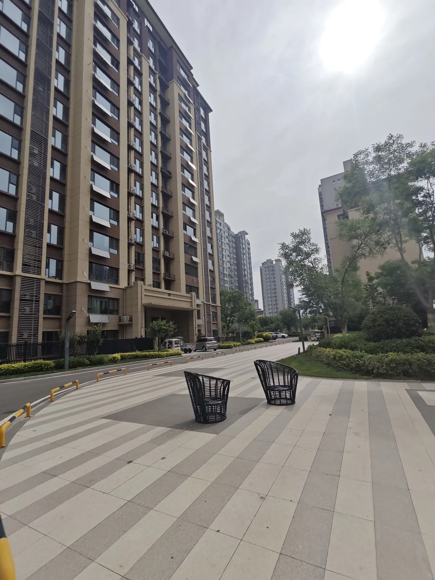 一栋多层现代风格的住宅建筑立面占据画面主体，外墙采用浅色调，设有多个窗户。建筑前方有铺设整齐的街道和低矮的绿化带，整体呈现出城市住宅区的现代居住氛围。