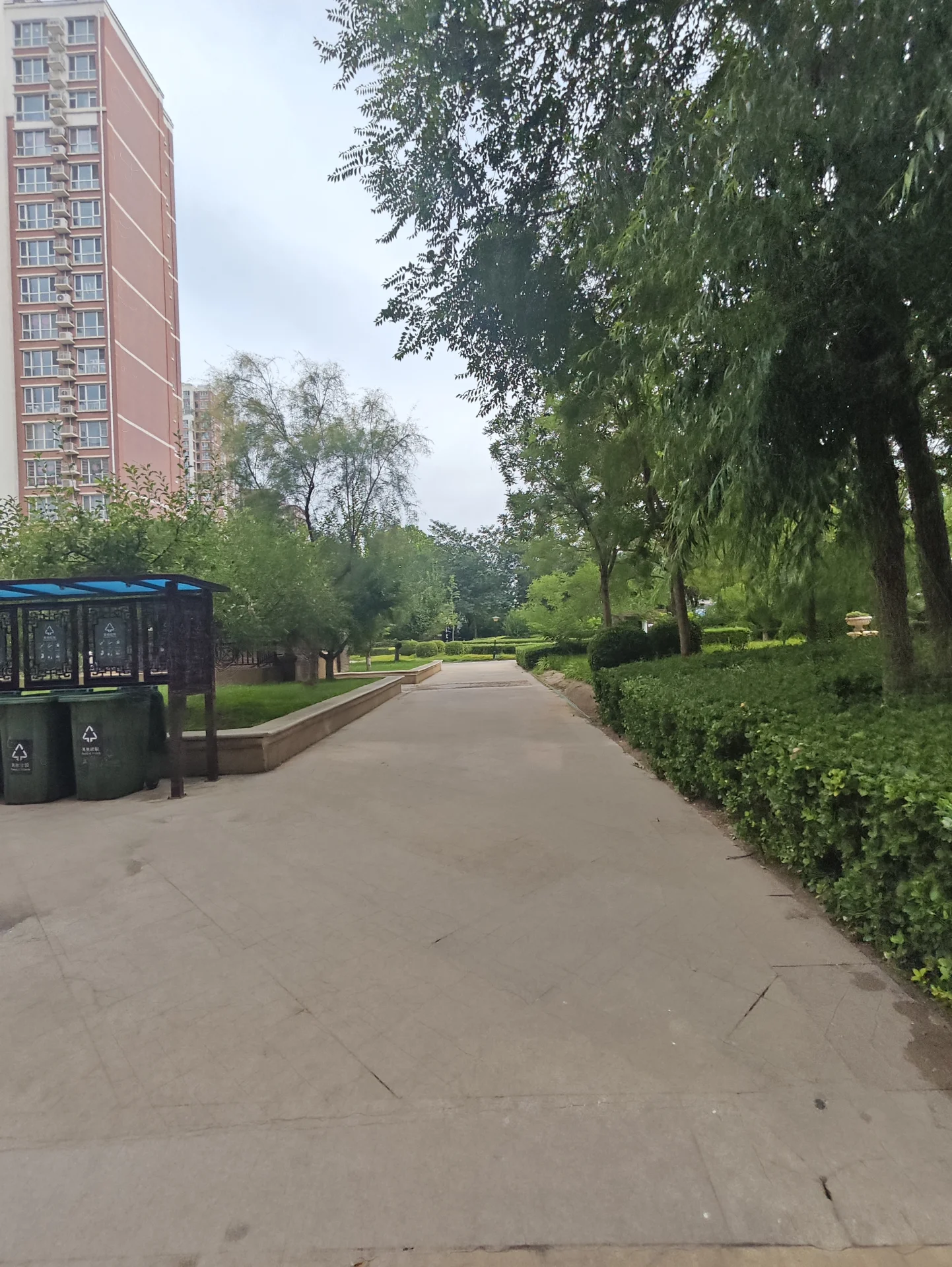 一栋高层住宅楼的立面清晰可见，建筑主体呈浅色调，周围环绕着茂密的绿化带和公共道路，整体呈现出社区建筑的宁静和谐氛围。