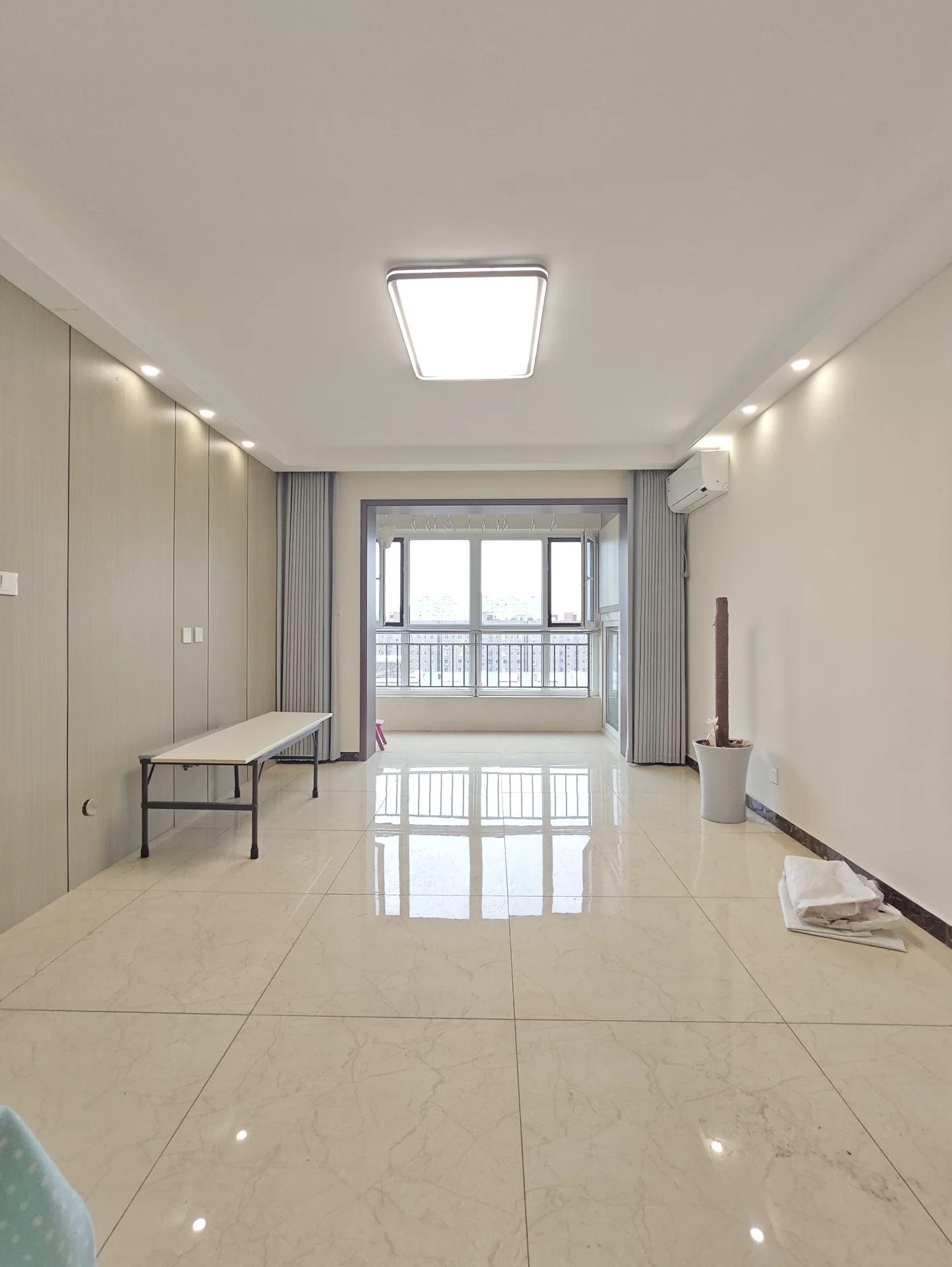 一个宽敞的室内空间，地面铺设米色大理石瓷砖，天花板采用嵌入式照明，空间光线明亮，整体呈现现代简约的居住环境。