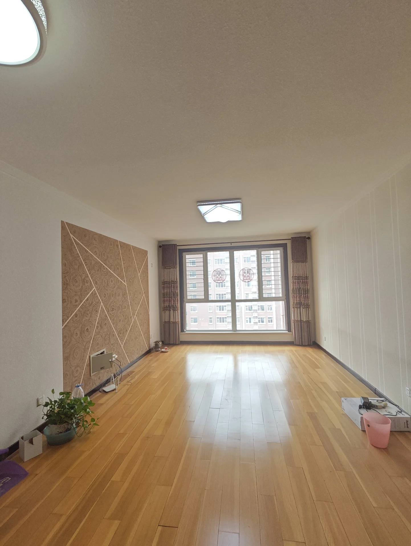 一个宽敞的室内空间，地面铺设了浅色木纹地板，墙面采用米色或浅色调，采光良好，空间布局开阔，整体呈现简洁明亮的居住环境。