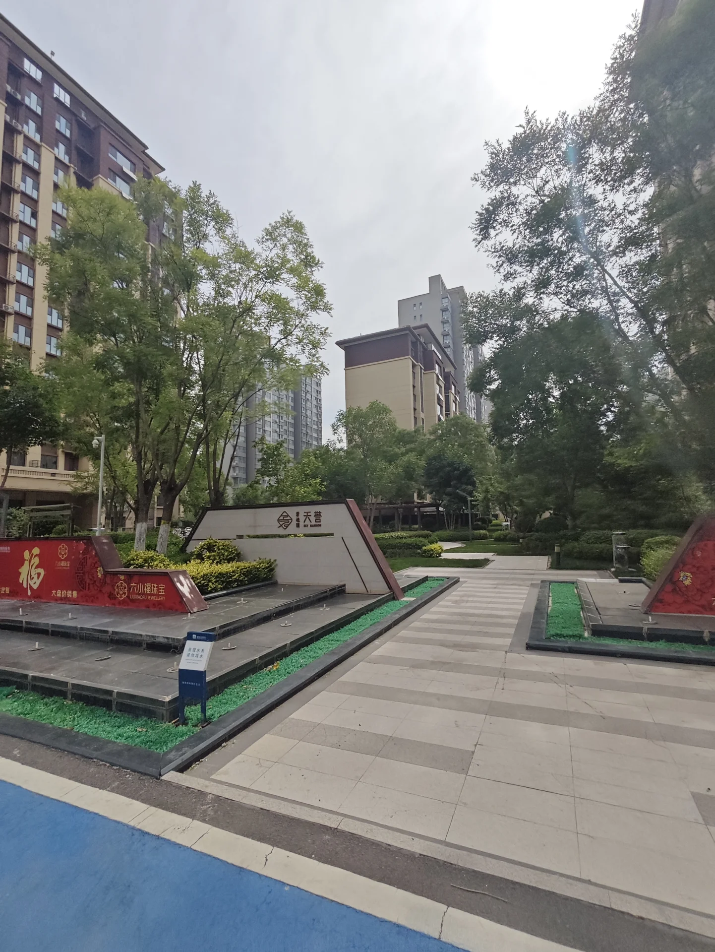 社区内部景观区域，绿化带和铺装步道构成了前景，背景是多栋高层住宅楼的外部立面，整体呈现出城市住宅区宁静和谐的氛围。