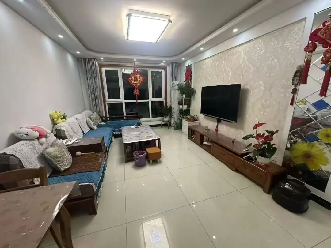 宽敞明亮的客厅，大窗户让自然光充分洒入。舒适的沙发、两把椅子和一张咖啡桌布置得井井有条。电视挂在沙发上方的墙上。瓷砖地板增添了一丝优雅。白色墙壁营造出清新明亮的氛围。现代简约风格，以中性色调和 contemporary 家具为主，整体和谐美观。