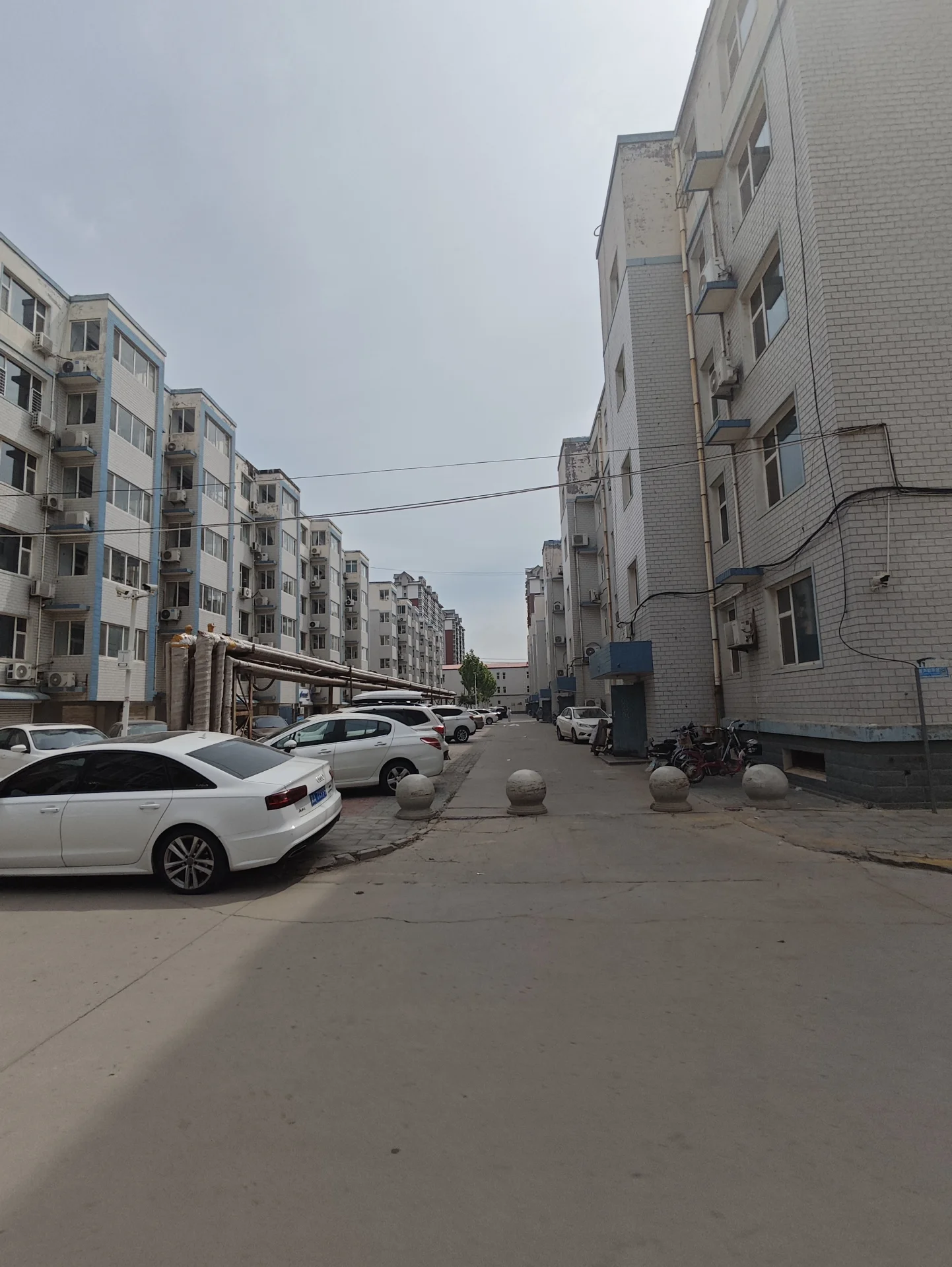 宁静的住宅街道，两侧是高大的砖墙建筑。路边停着几辆车，有人在街上行驶或在人行道上散步。整体氛围平静，没有交通拥堵的迹象。建筑风格融合了现代和传统元素，显得非常和谐。关键字:住宅街道 砖墙建筑 宁静氛围 现代传统元素