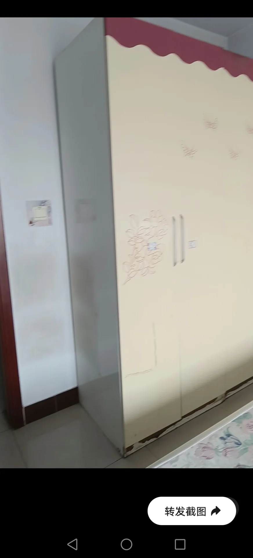 图片展示一个白色房间，窗帘是粉色和白色条纹的。房间一侧墙壁上有一个白色衣柜，窗户很小。房间看起来像卧室，床放在角落里。整体氛围显得平静祥和，房间的色彩方案营造出温暖舒适的感觉。