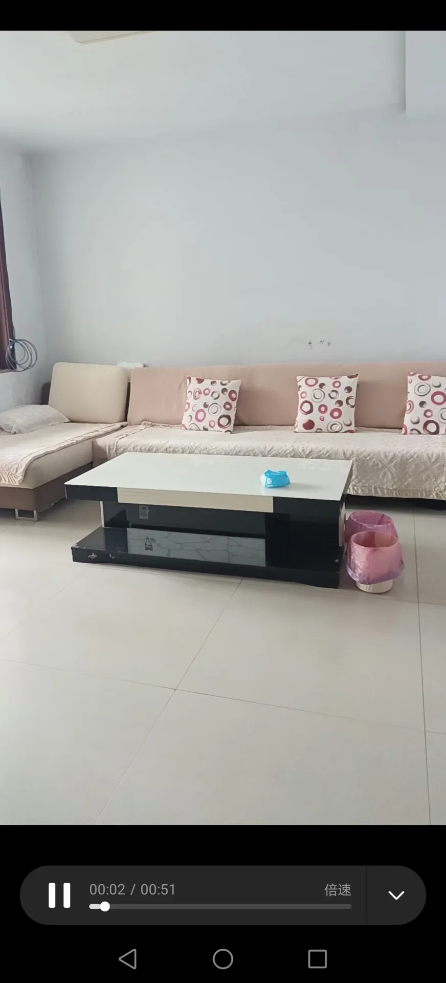 图片展示了一个带有白色桌子的客厅，桌子上放着一个粉色和白色的抱枕，以及一个蓝色的杯子。房间看起来干净整洁，色彩以中性色为主。沙发靠墙摆放，整体氛围显得平静而温馨。