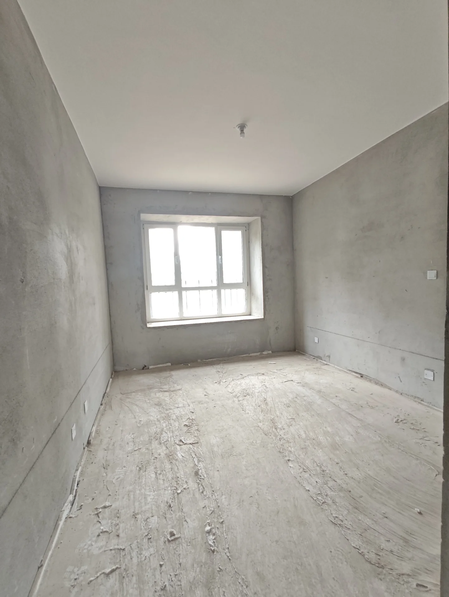 空房间，地面为混凝土，无家具，有窗户引入自然光，墙壁白色，空间空旷简洁。