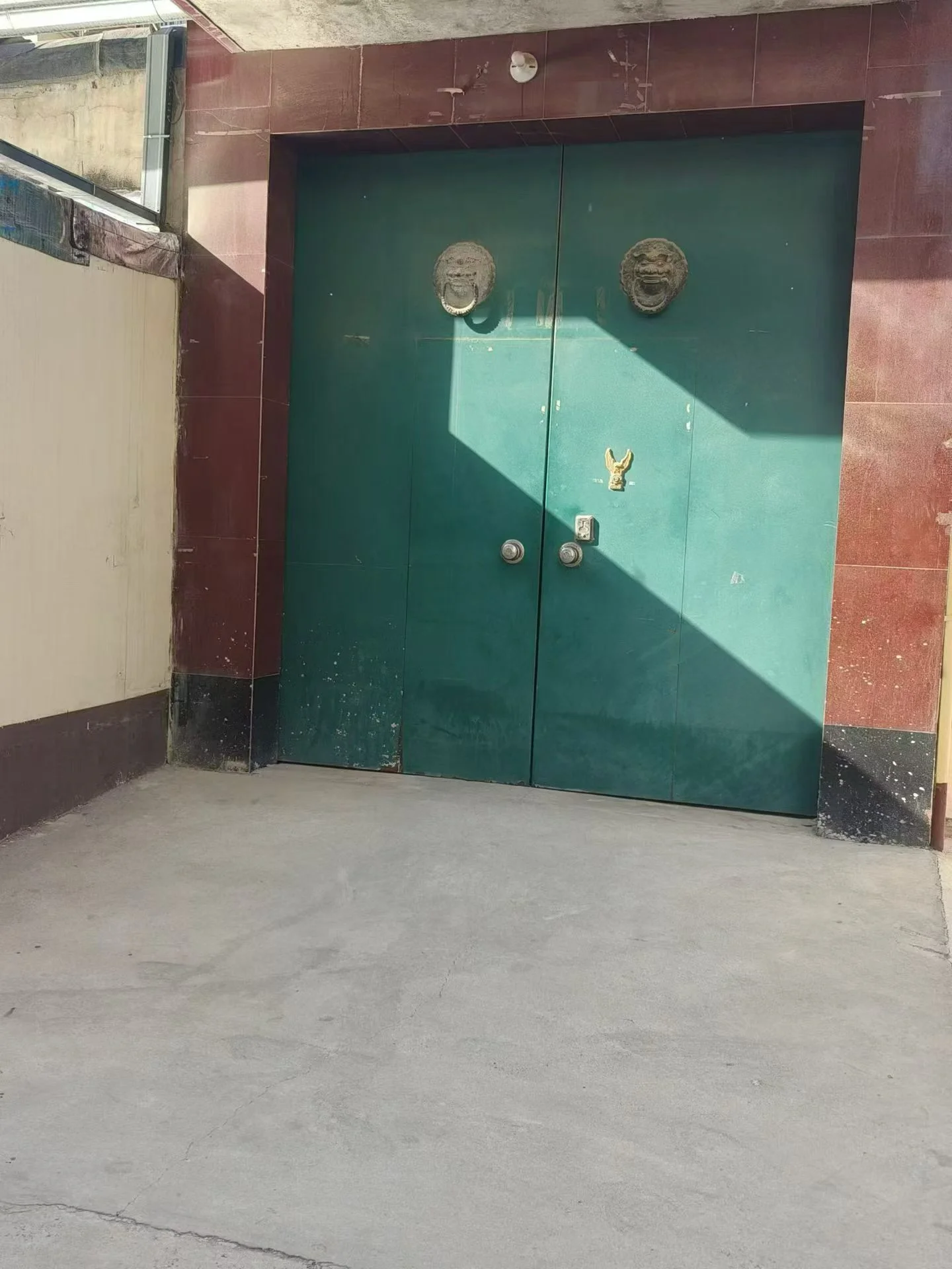 绿门建筑前，金属门敞开，人行道旁安静祥和，独特风格凸显。关键字:绿门 金属门 人行道 安静祥和 独特风格