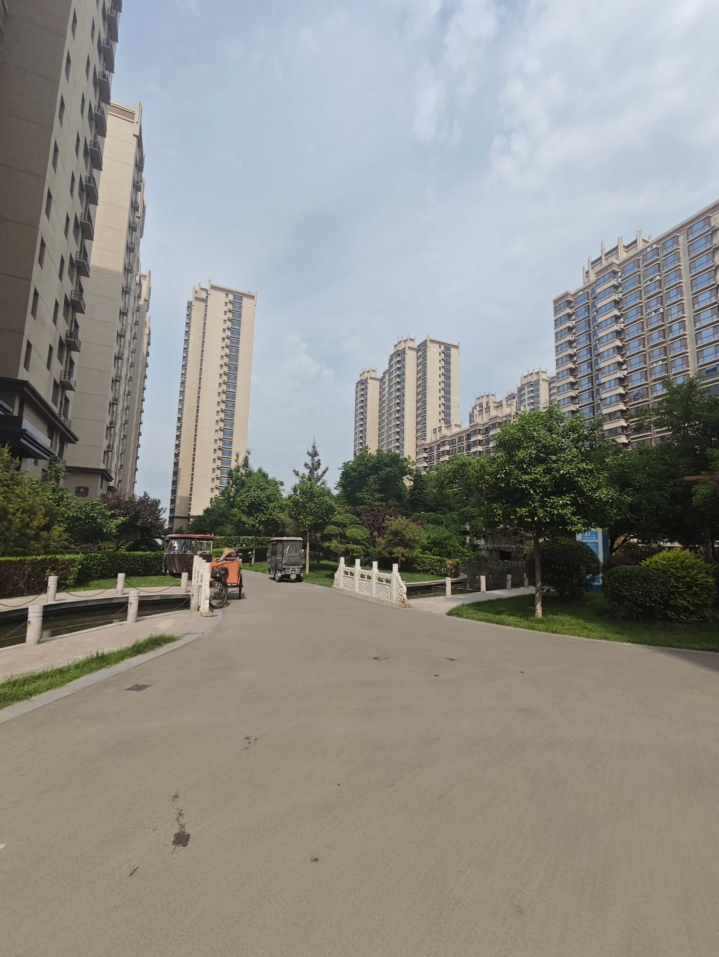 城市街道两旁高楼林立，营造出繁华都市氛围。街道两侧绿树成荫，长椅点缀其间，为喧嚣环境增添一抹绿意和放松气息。道路上停放着多辆汽车，显示此地人流量较大。一辆卡车出现在画面中，进一步凸显城市的活力。建筑风格现代，高耸 sleek，整体捕捉到一个充满活力的都市景象，人们在这里忙碌或享受闲暇时光。关键字:城市街道 高楼 绿树 长椅 汽车 卡车 现代建筑